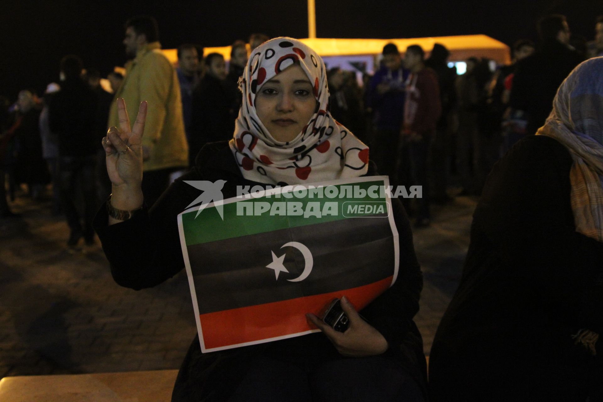 Бенгази. Гражданская война в Ливии - `Арабская весна`. `Площадь Свободы`. Митинг оппозиции. На снимке: ливийская женщина держит плакат с изображением национального флага и демонстрирует жест Victory (Победа).