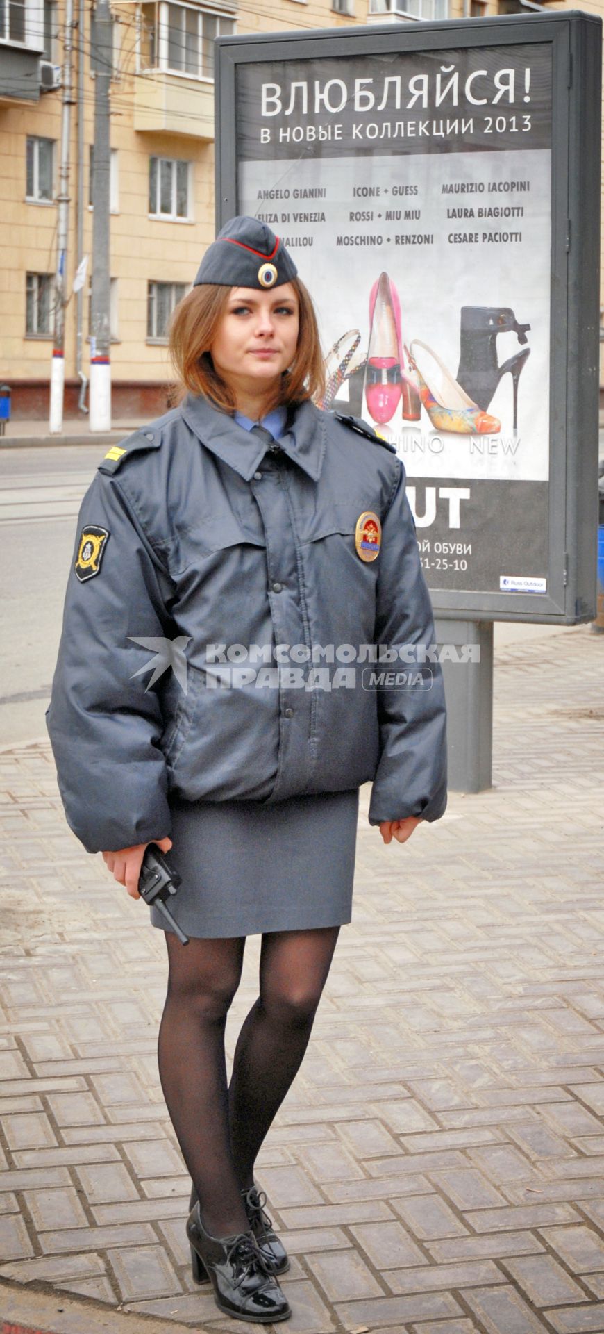 Женщина полицейский стоит на фоне плаката с надписью `Влюбляйся`.