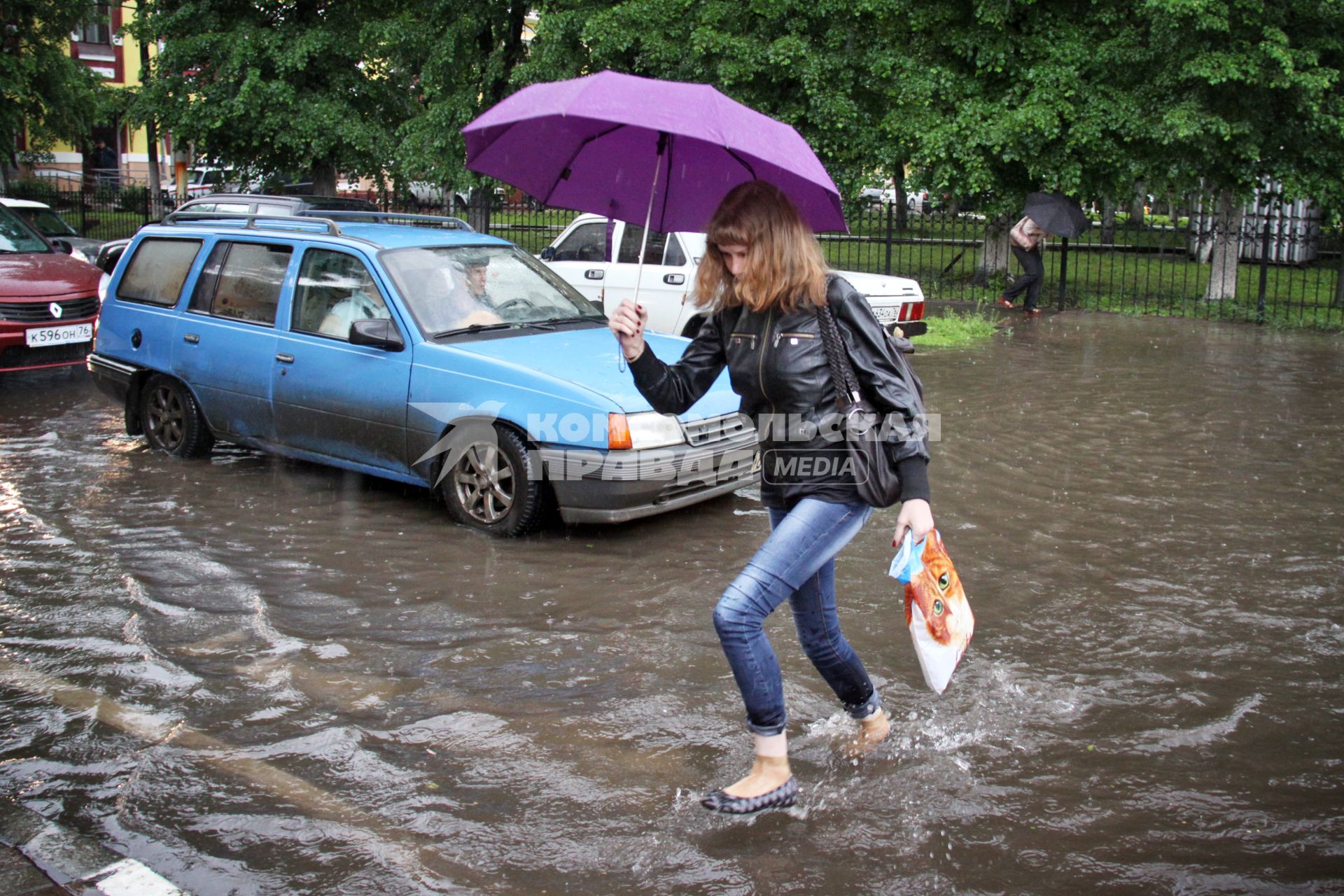 Последствия ливня в городе - затопленные улицы. Девушка под зонтом переходит затопленную улицу.