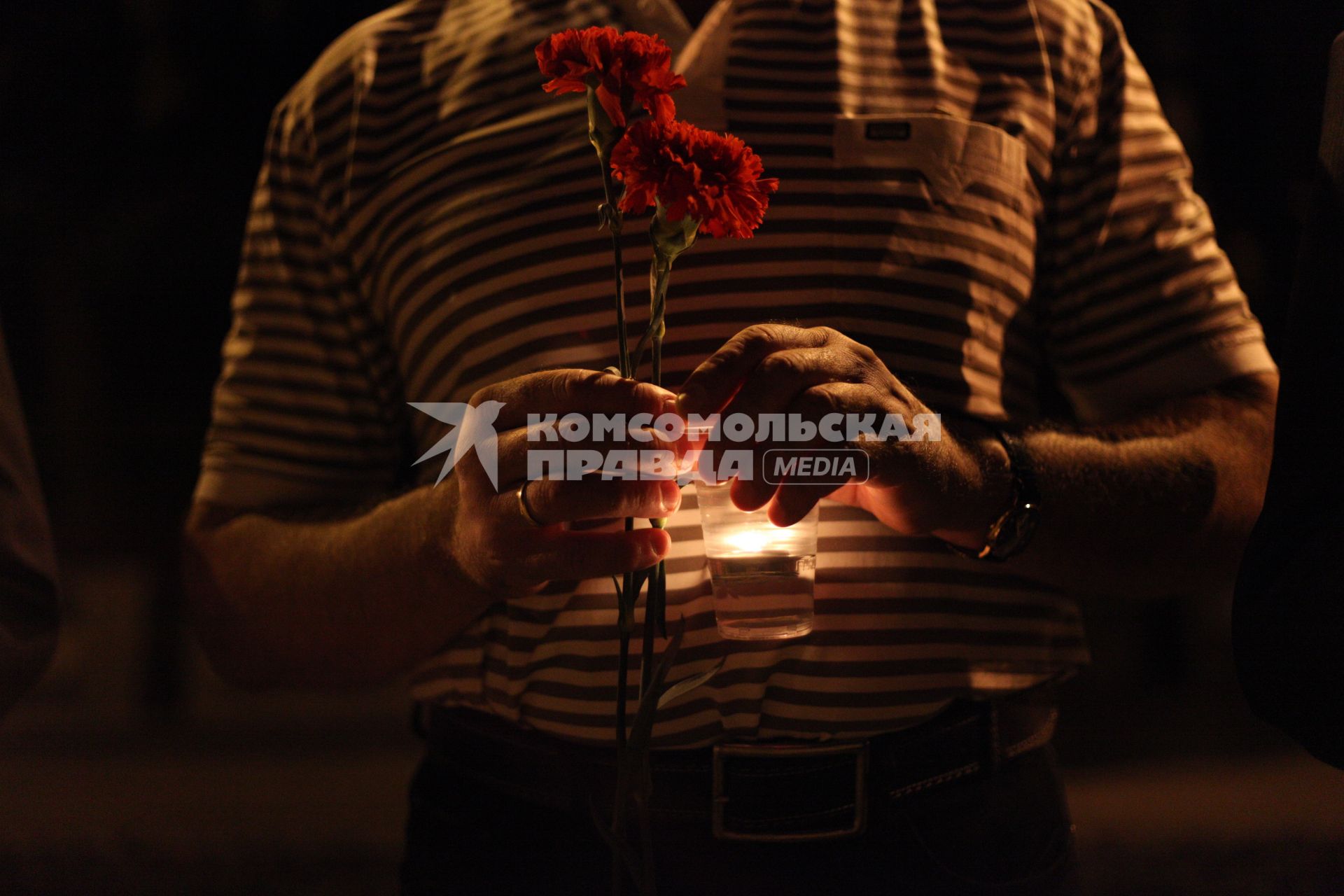 Мужчина держит в руках стаканчик со свечой и гвоздики