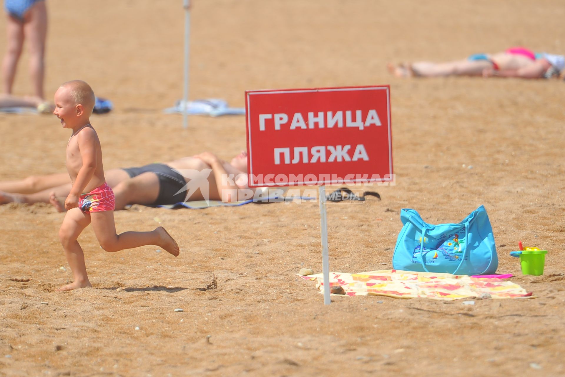 Отпуск на море. На снимке: ребенок бежит у таблички `Граница пляжа`