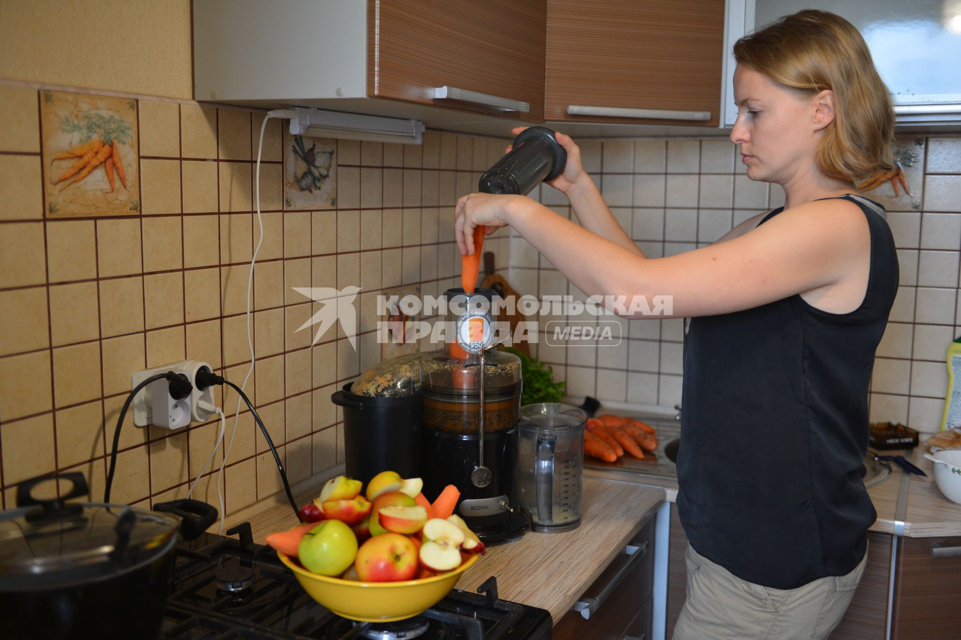 Девушка готовит свежевыжатый сок из яблок и моркови.