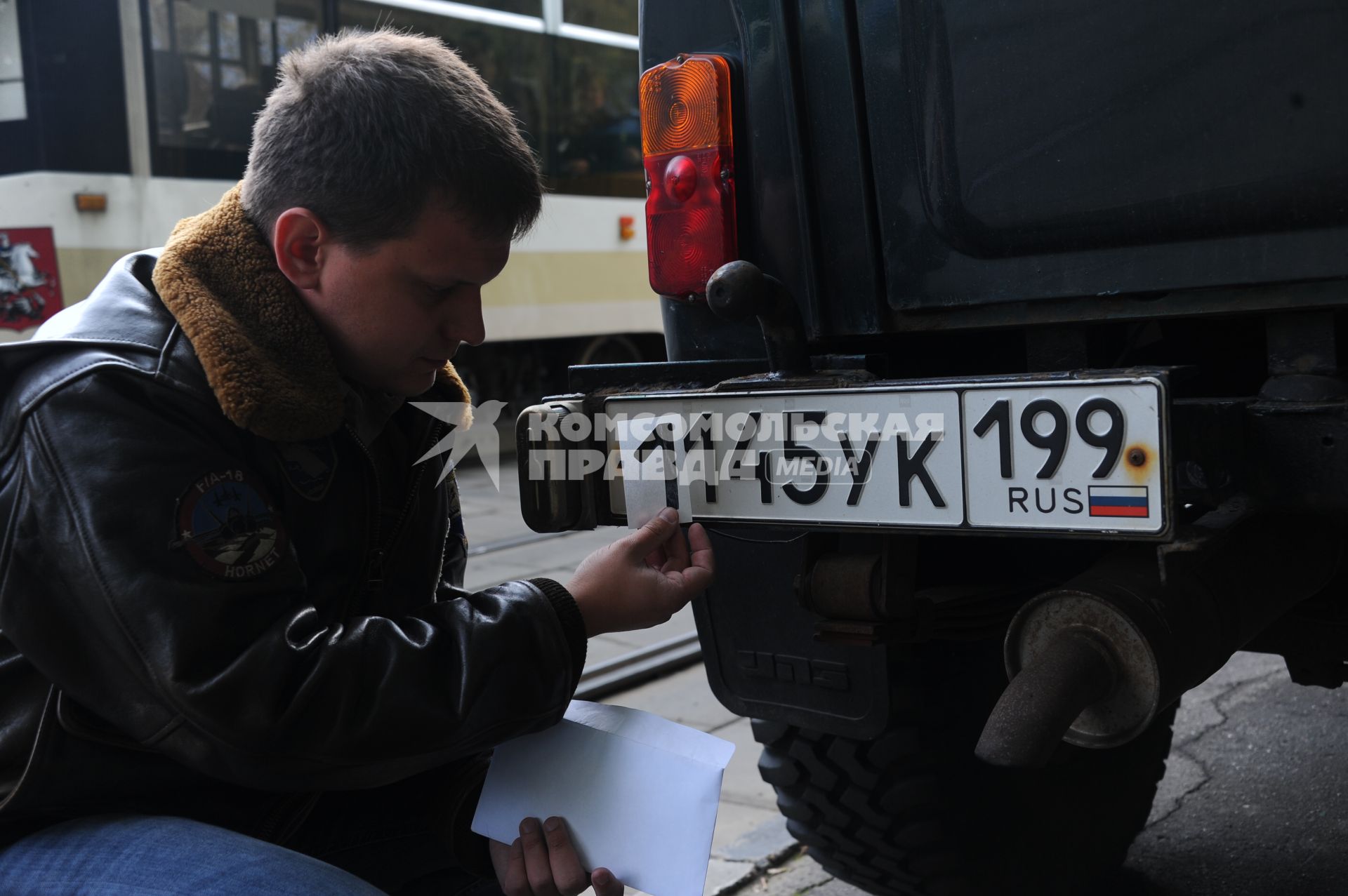 Мужчина наклеивает бумажные цифры на автомобильный номер.