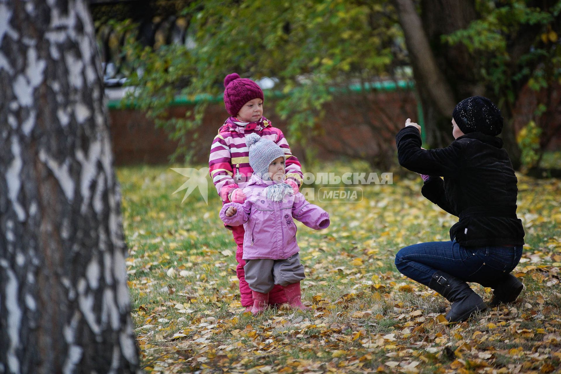 Женщина фотографирует детей в осеннем парке.