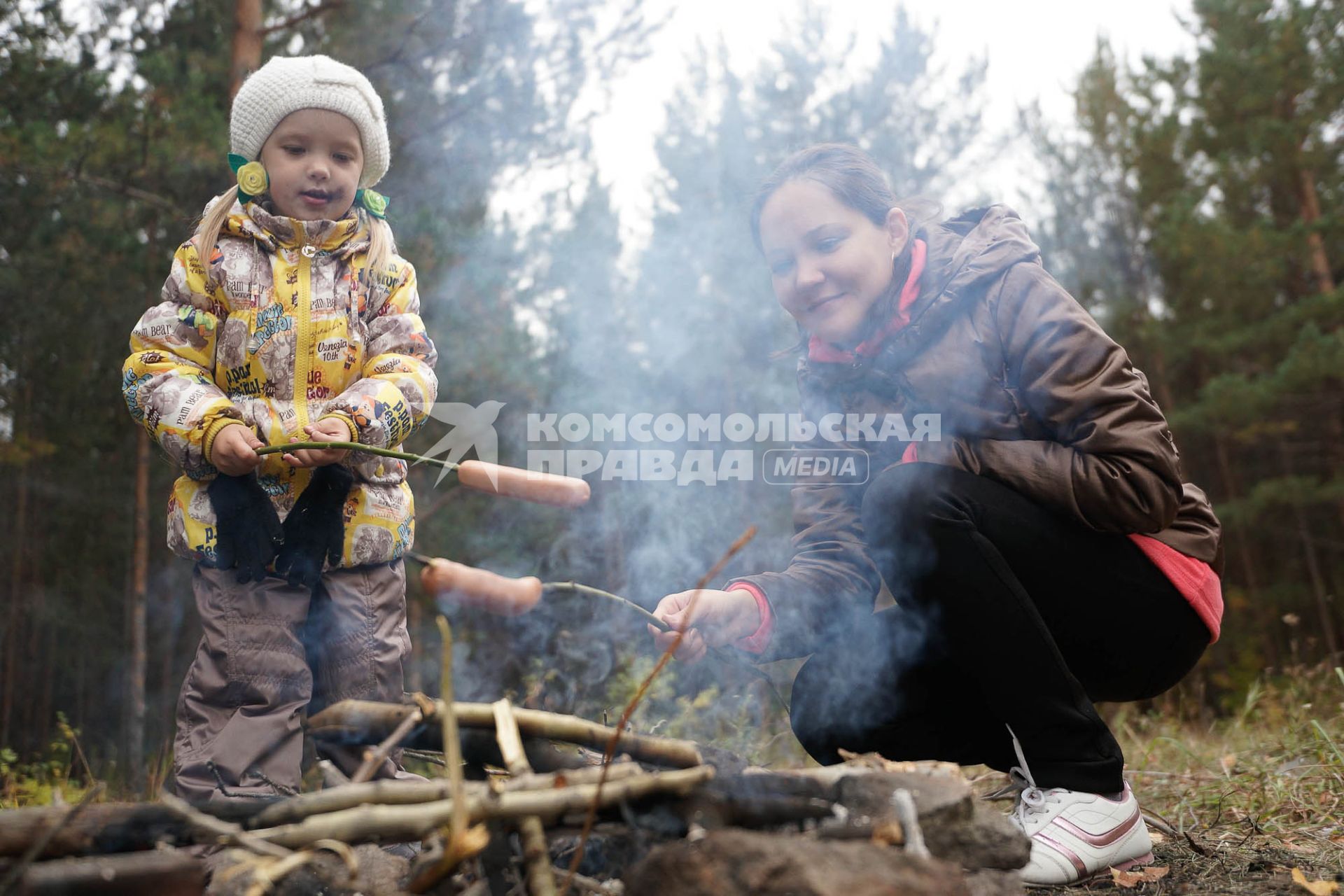 Женщина с ребенком жарят сосиски на костре.