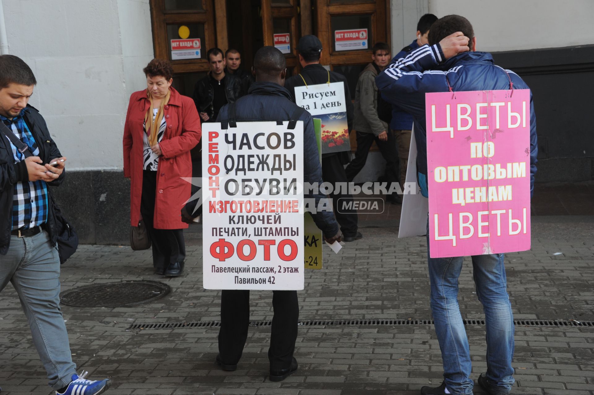 Живая реклама. На снимке:  мужчины с рекламными плакатами `Ремонт часов, одежды, обуви` и `Цветы по оптовым ценам`