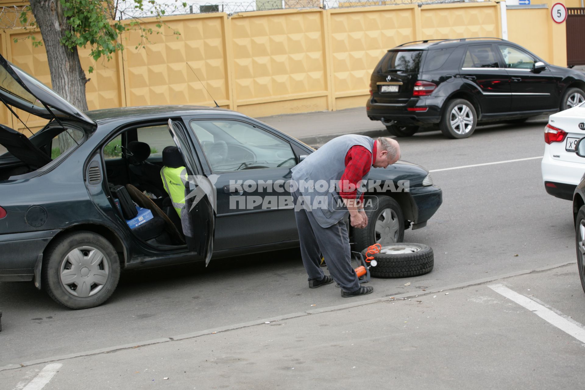 Ремонт автомобиля. На снимке: мужчина качает автомобильную шину ножным насосом.