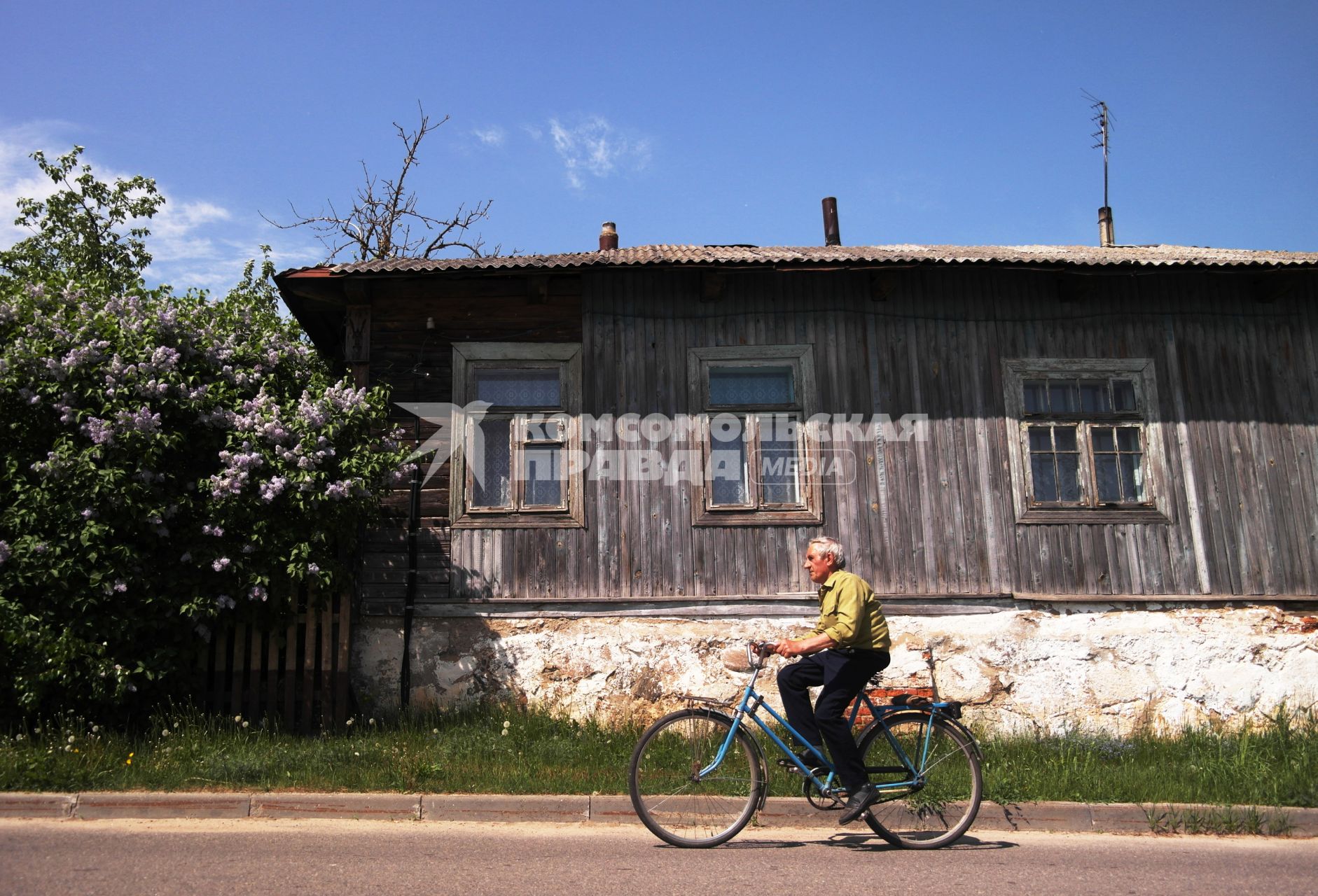 Мужчина едет на велосипеде возле деревянного дома.