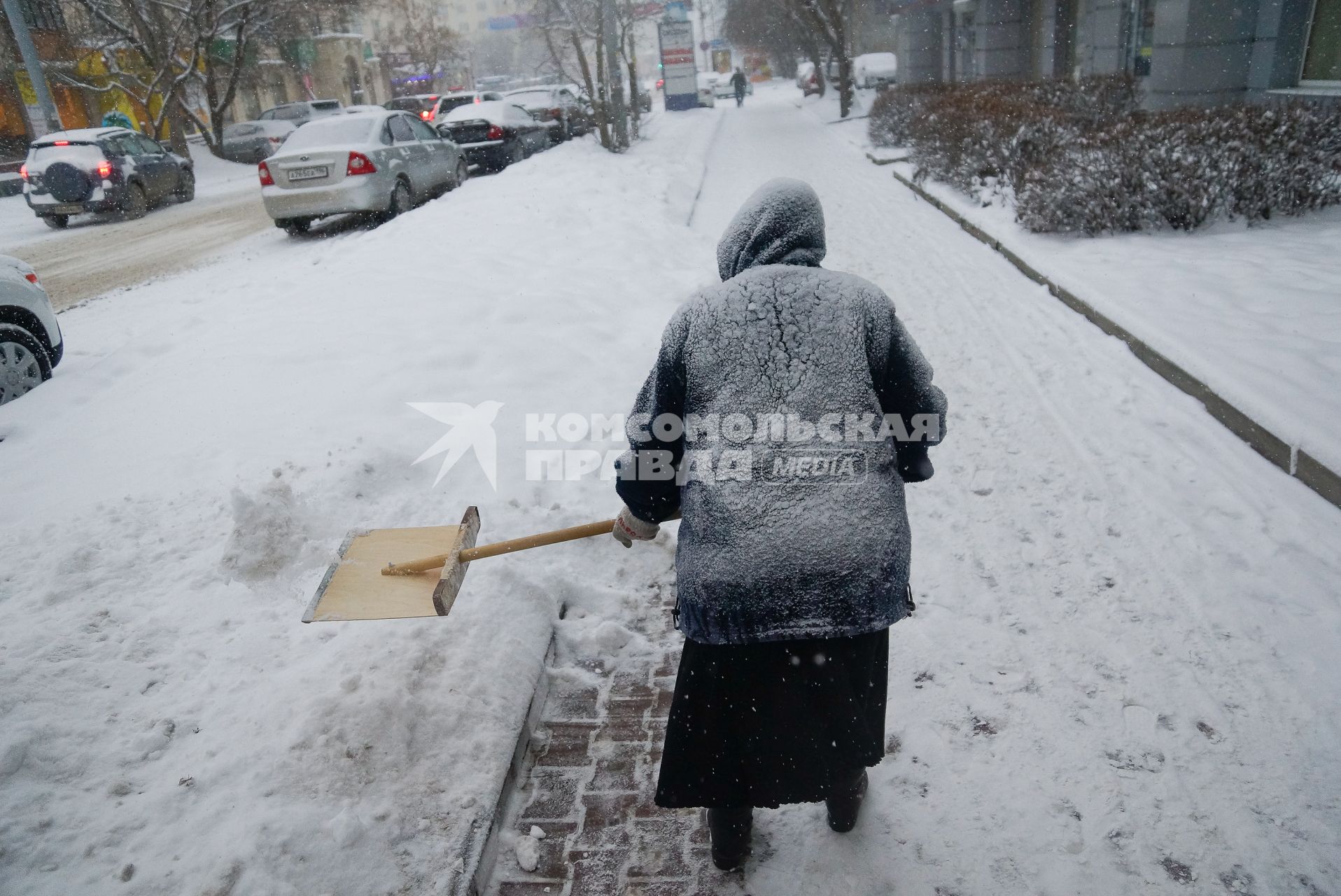 Снегопад в Екатеринбурге. На снимке: женщина убирает снег с пешеходной зоны деревянной лопатой.