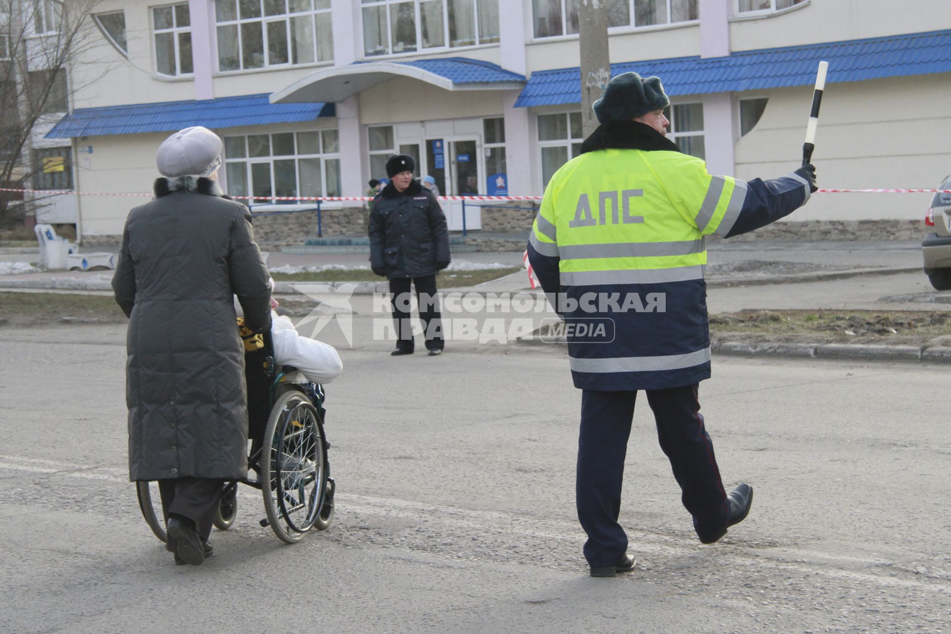 Сотрудник ГИБДД помогает перейти дорогу женщине везущей инвалида в коляске.