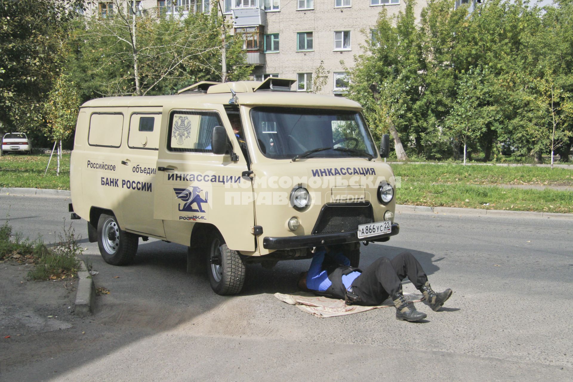 Инкассаторский автомобиль сломался. Водитель лежит под машиной и ремонтирует.