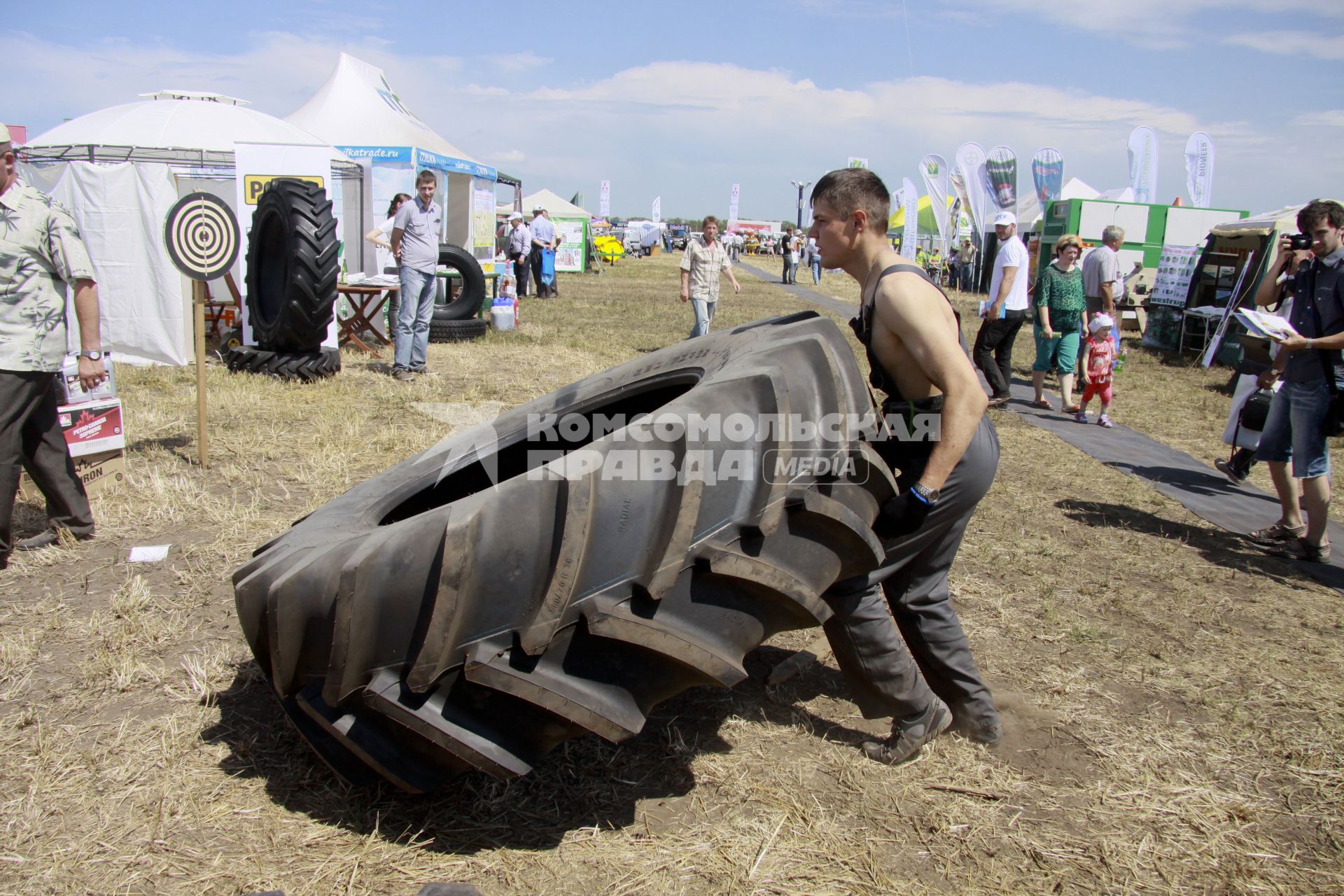 Межрегиональный агропромышленный форум `День сибирского поля - 2013`. Конкурс силачей. Мужчина поднимает огромное колесо.