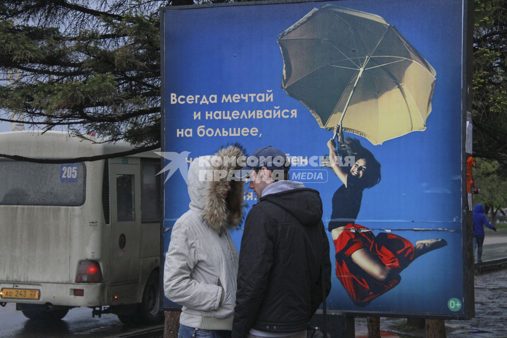 Юноша и девушка разговаривают на улице напротив рекламы с надписью: `Всегда мечтай и нацеливайся на большее`.