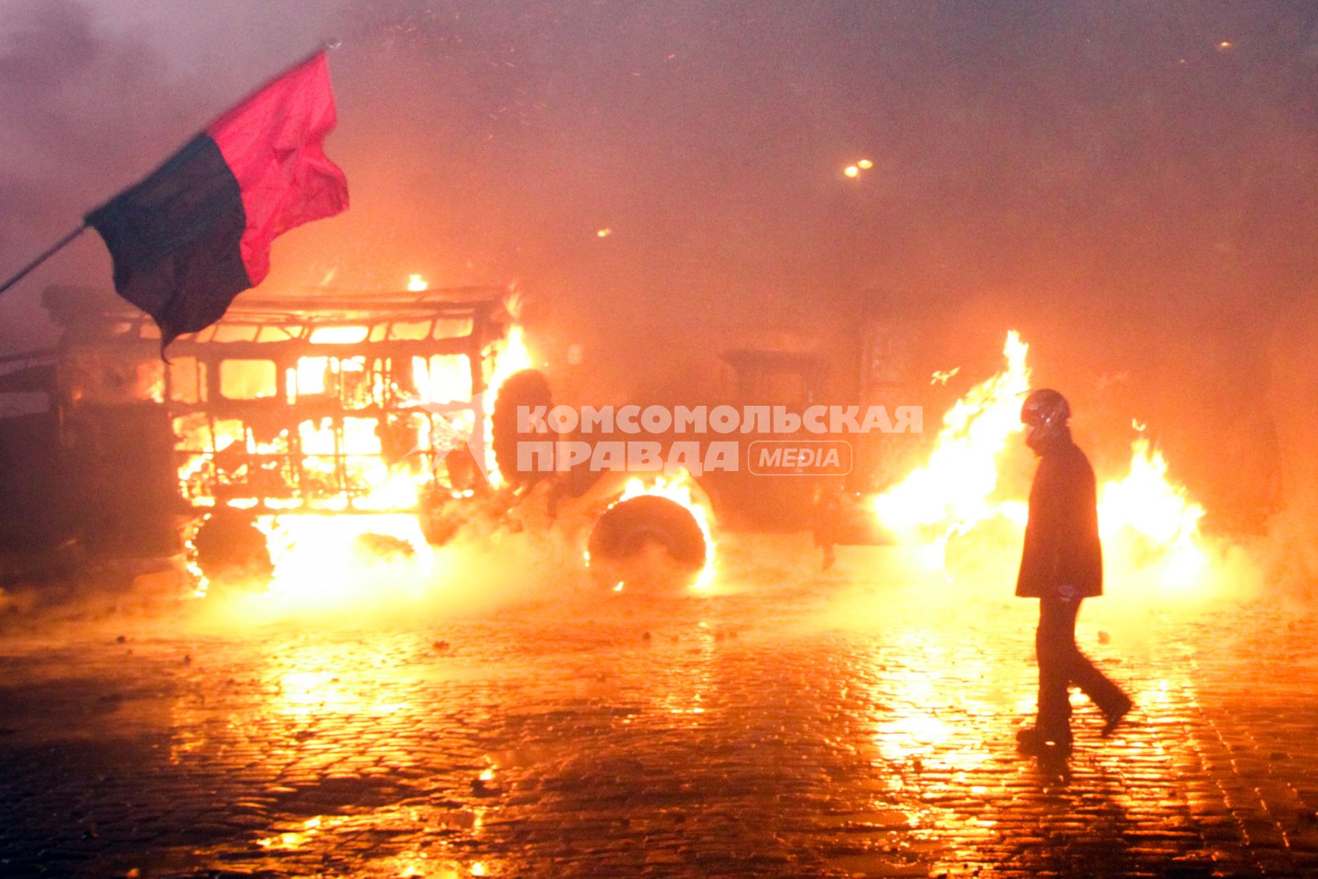 Протестующий в шлеме на фоне горящего автобуса.