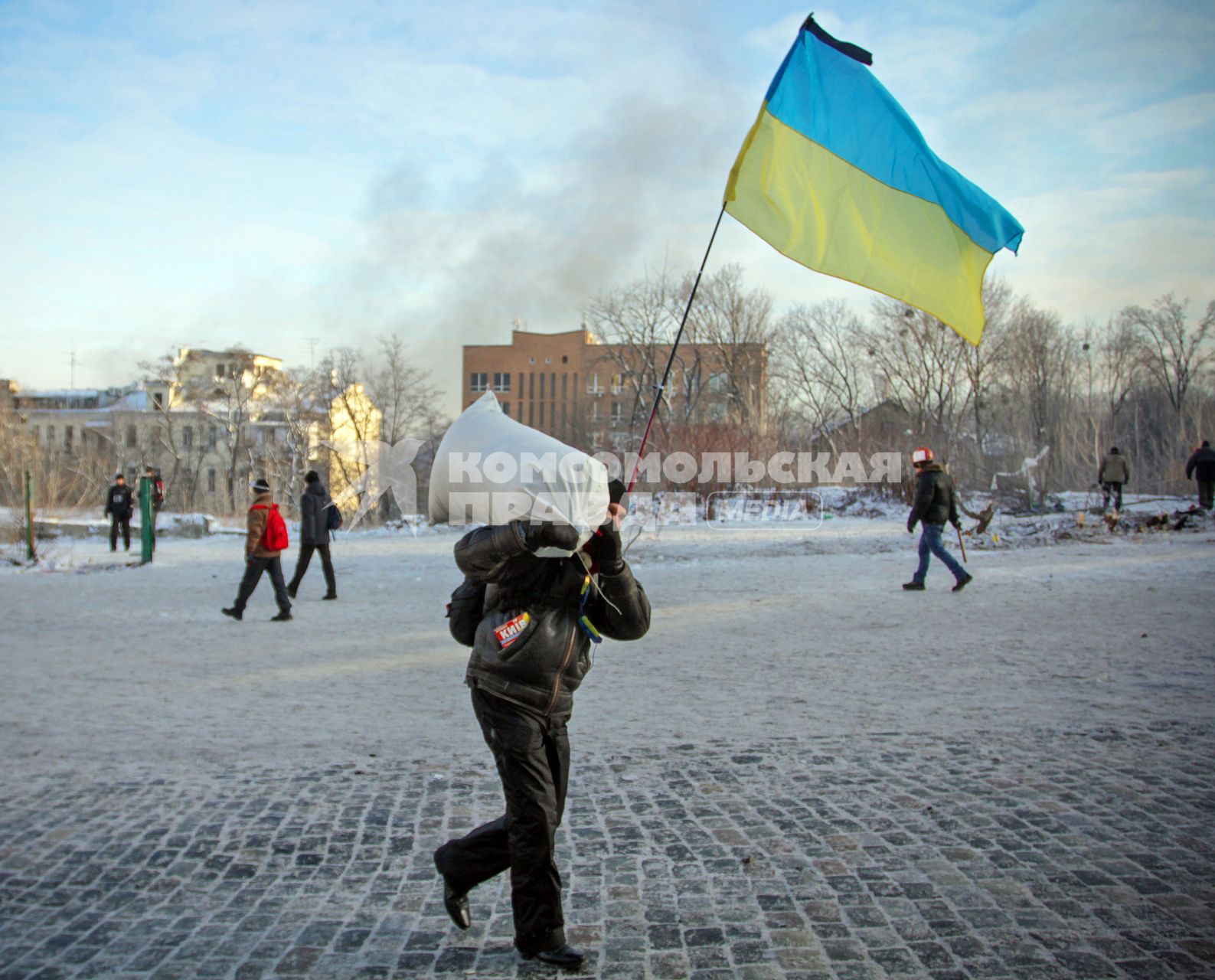 Протестующий с украинским флагом несет мешок для укрепления баррикад.