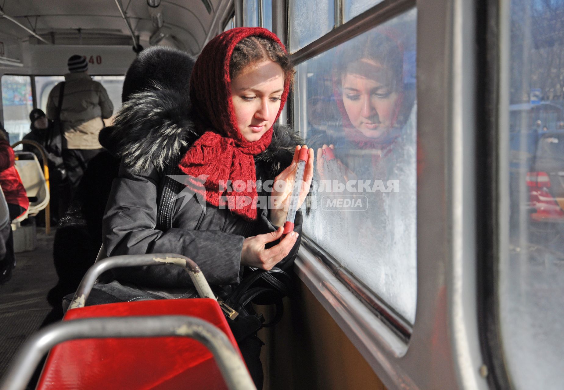 Девушка в общественном транспорте с градусником в руках.