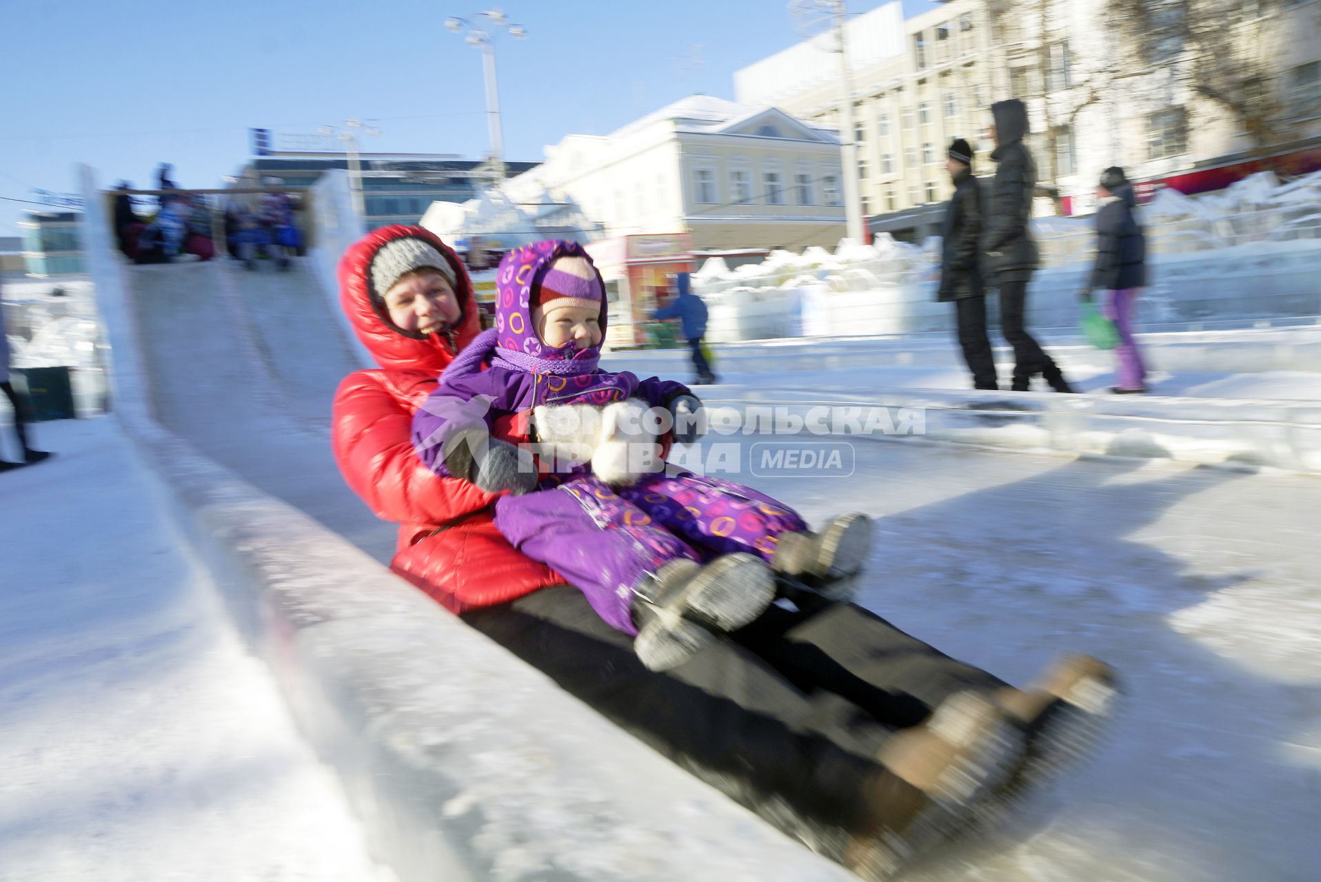 Женщина с ребенком катается на ледяной горке.