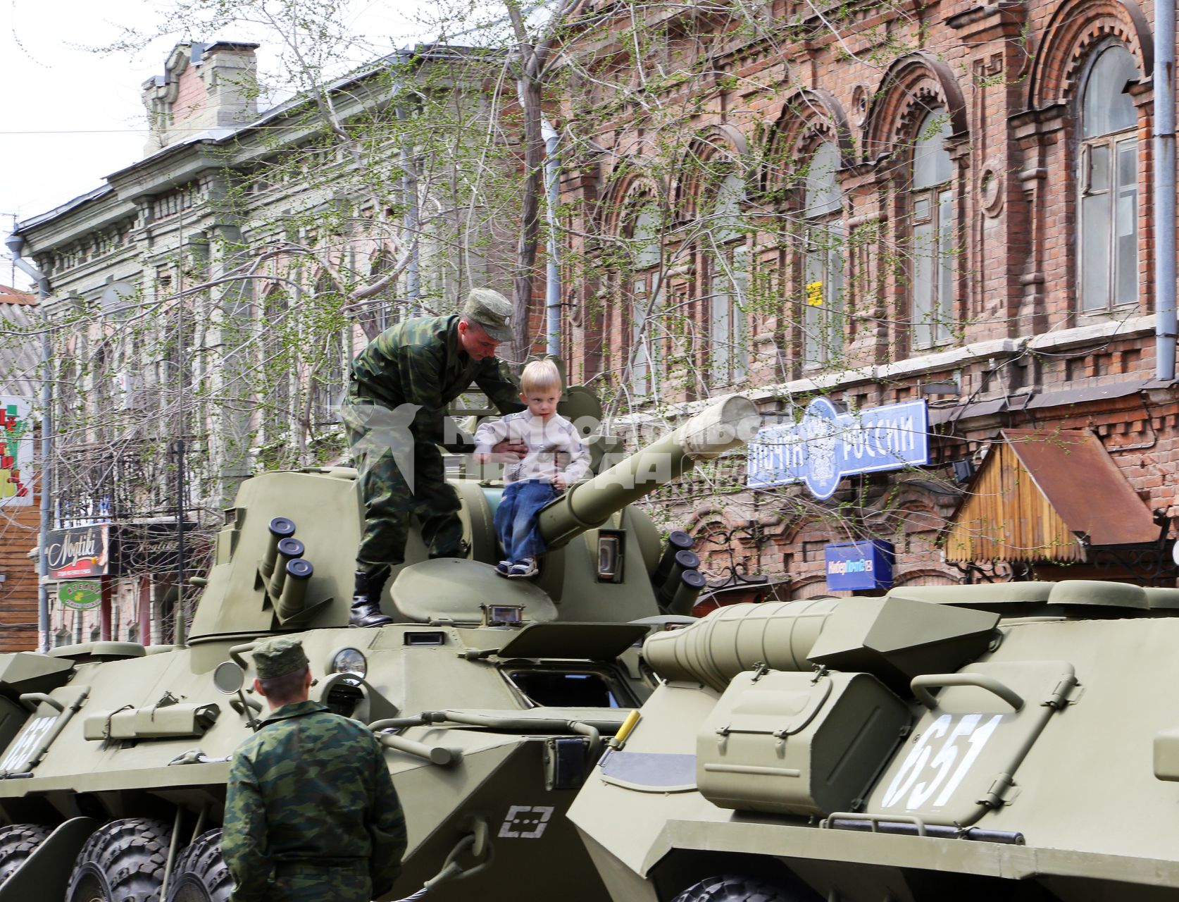 Перед Парадом Победы военная техника дислоцируется на улицах города. Солдат усаживает ребенка на ствол орудия.