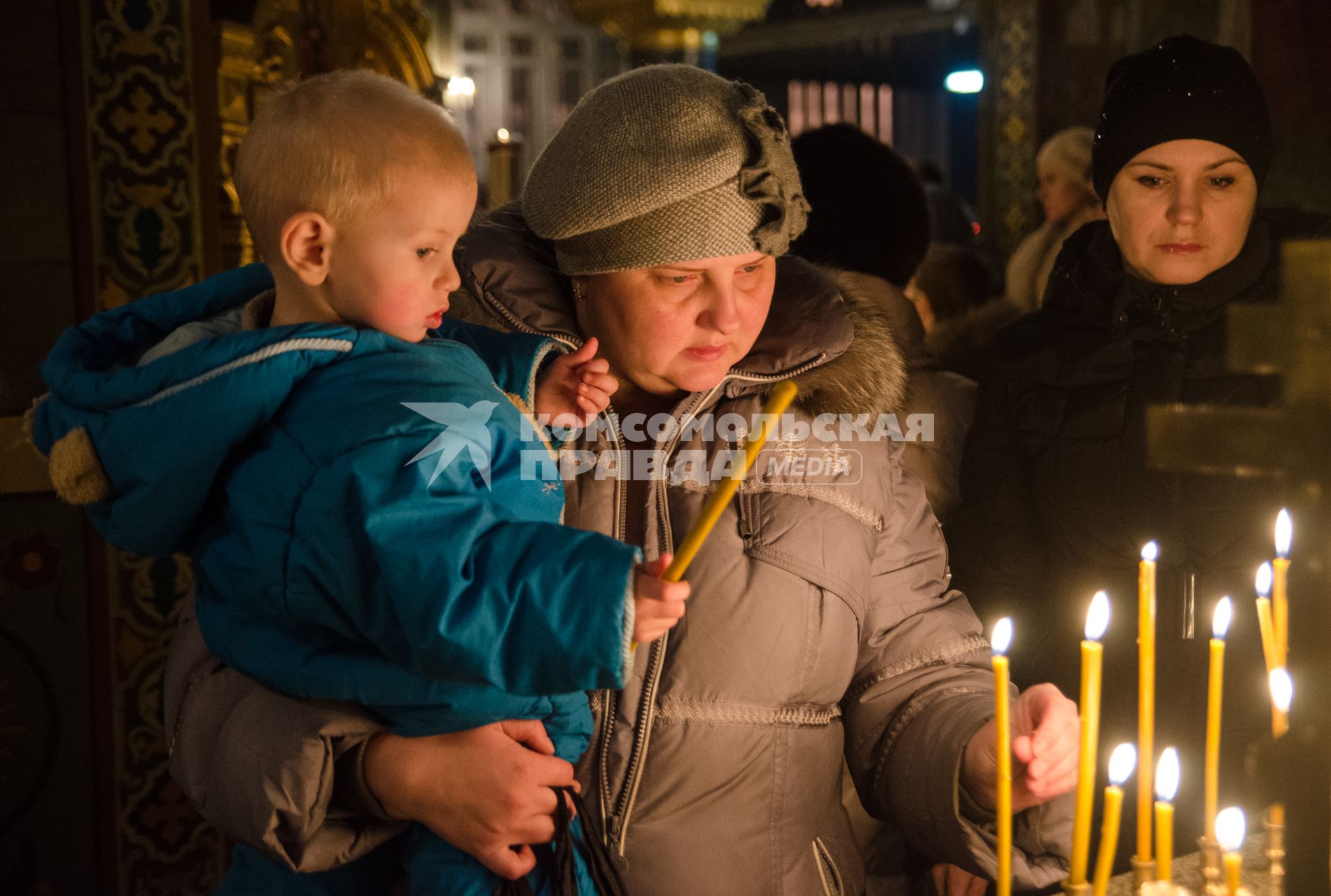 Крещение в Самаре. Женщина ставит свечку держа на руках ребенка.