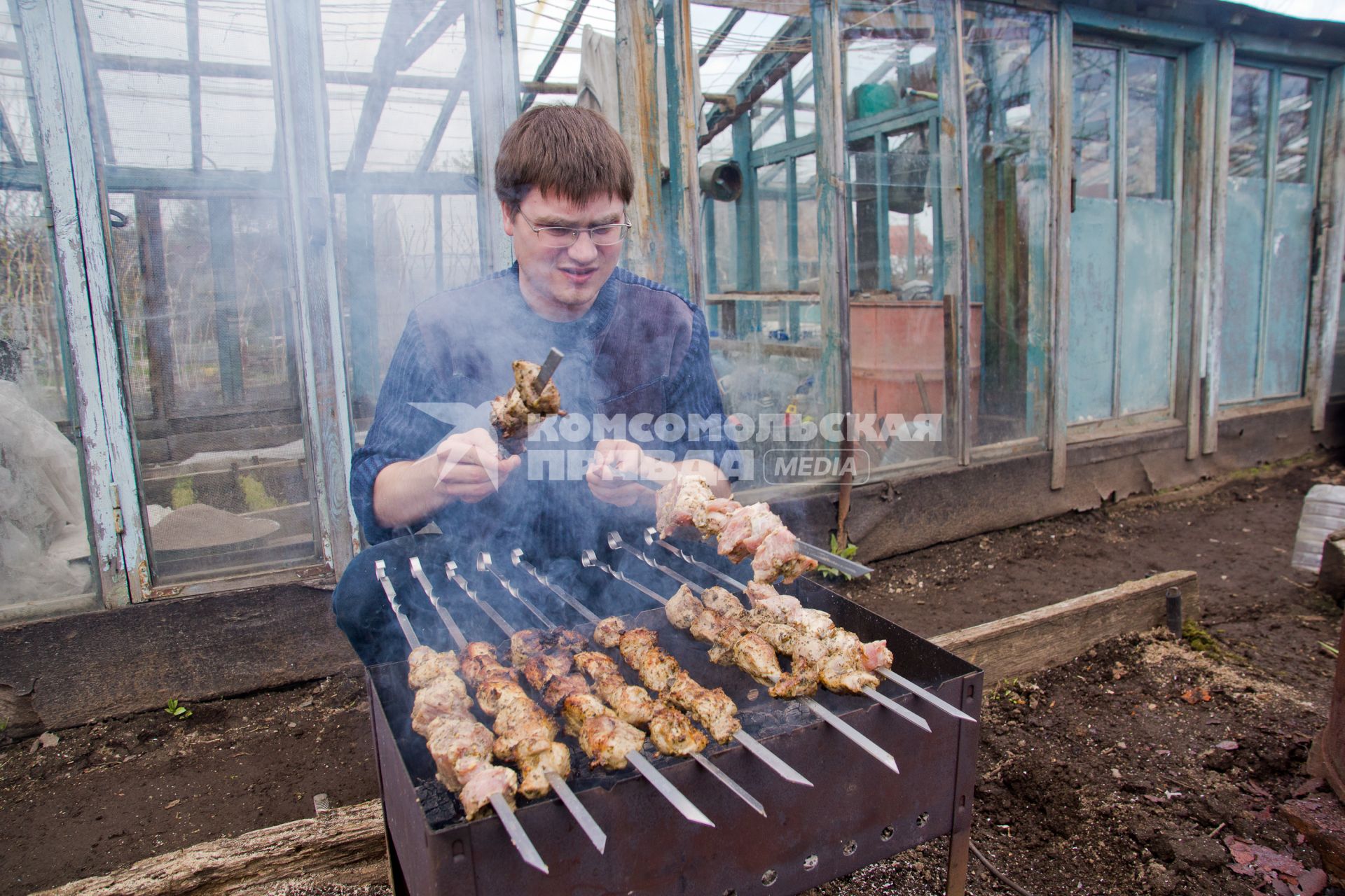 Мужчина жарит шашлыки на даче.