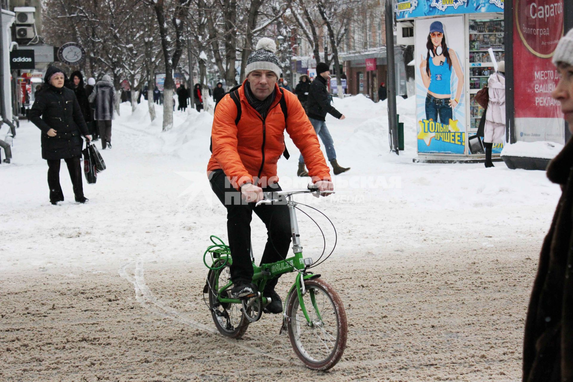 Мужчина на велосипеде едет по заснеженной улице.