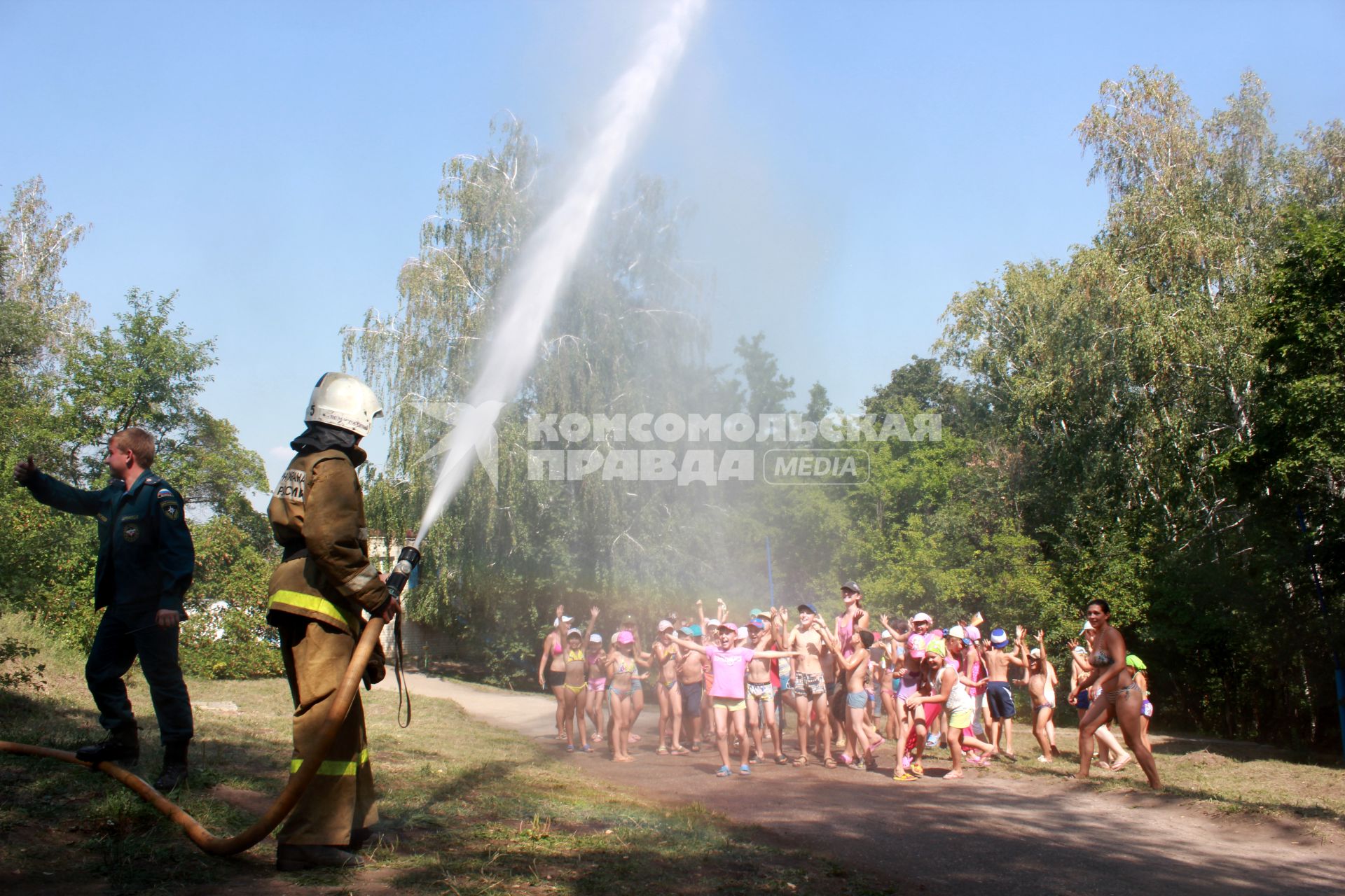 Пожарный обливает детей из пожарного шланга.