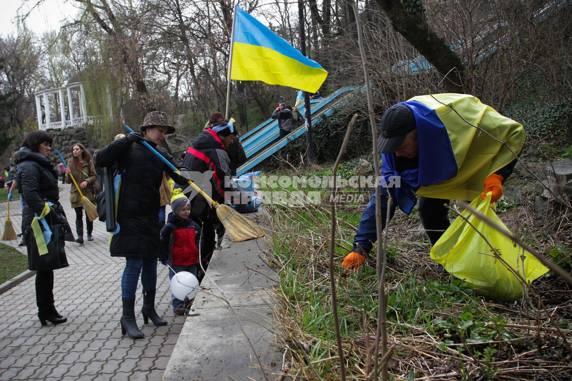 Люди убирают территорию парка под флагом Украины.