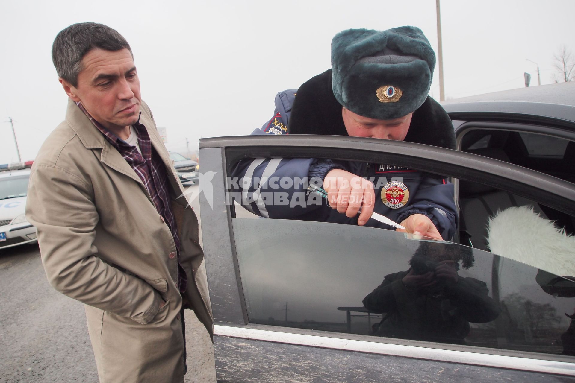 Сотрудник ДПС ГИБДД помогает отодрать тонировку.