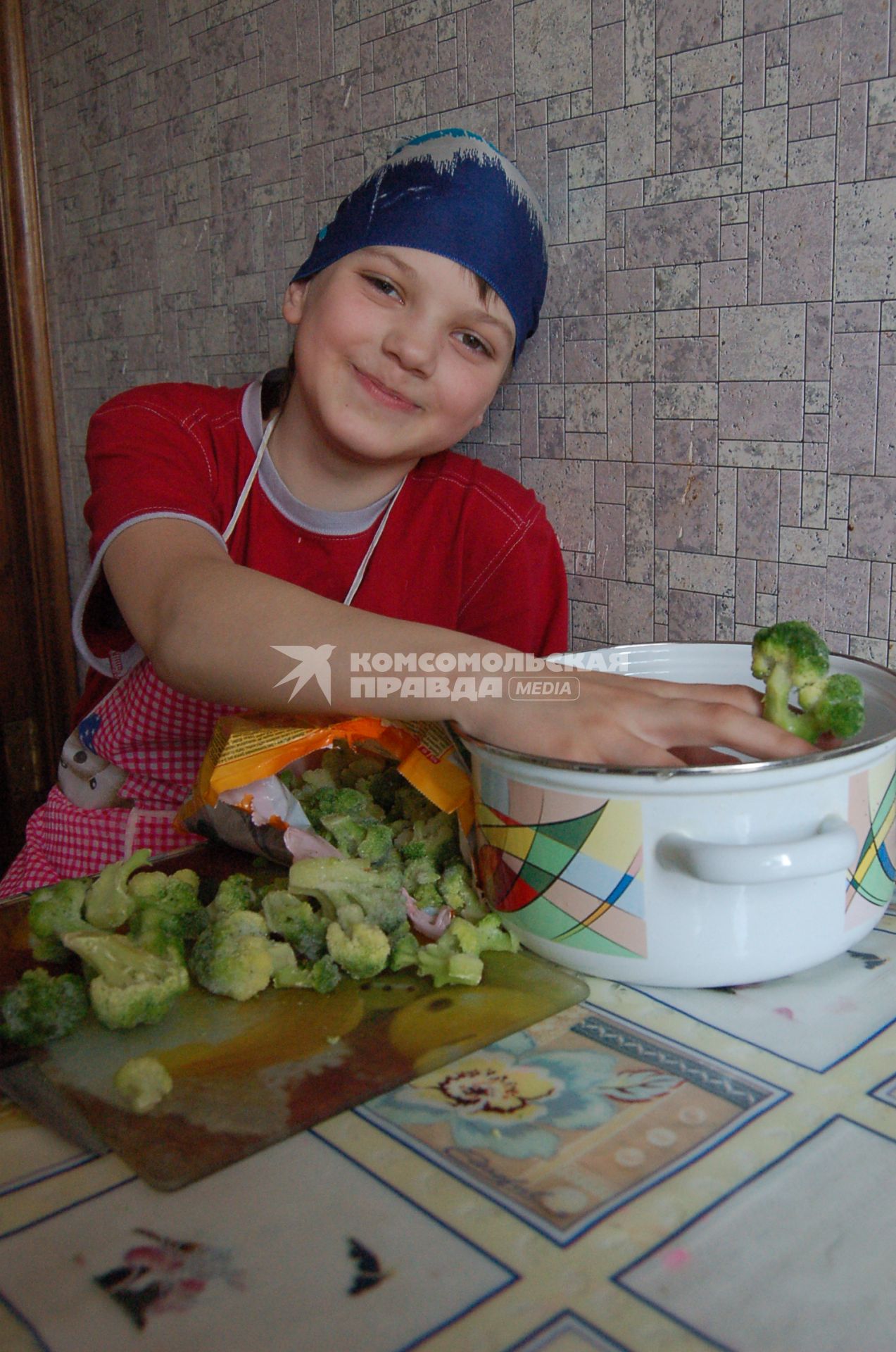 Мальчик на кухне с замороженной капустой брокколи.