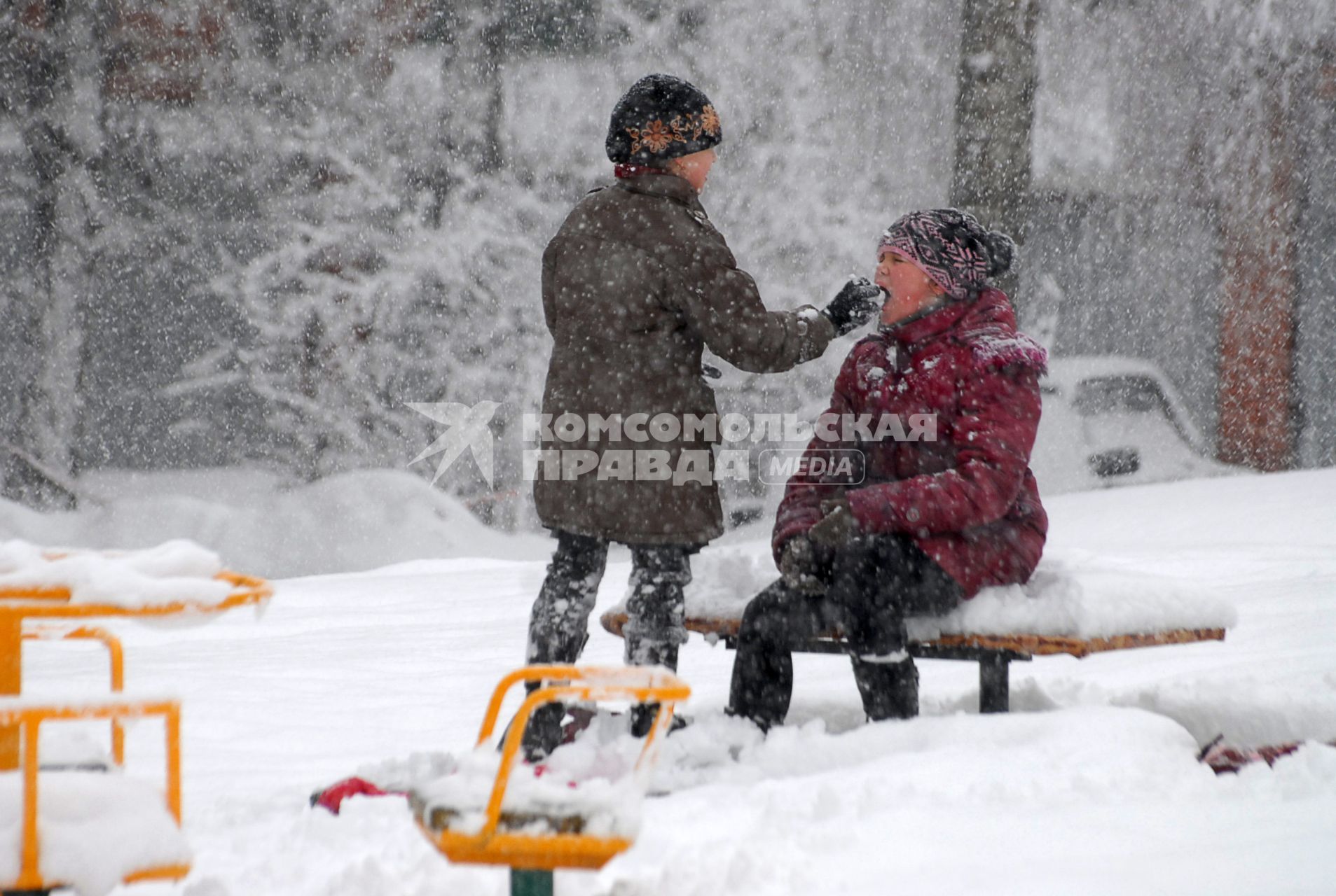 Дети на заснеженной детской площадке, под снегопадом.