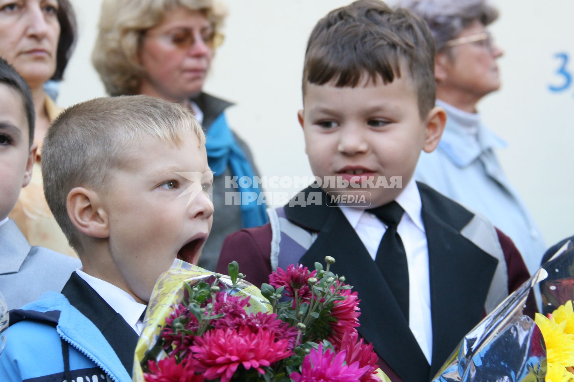 Зевающий ребенок с букетом цветов на школьной линейке.