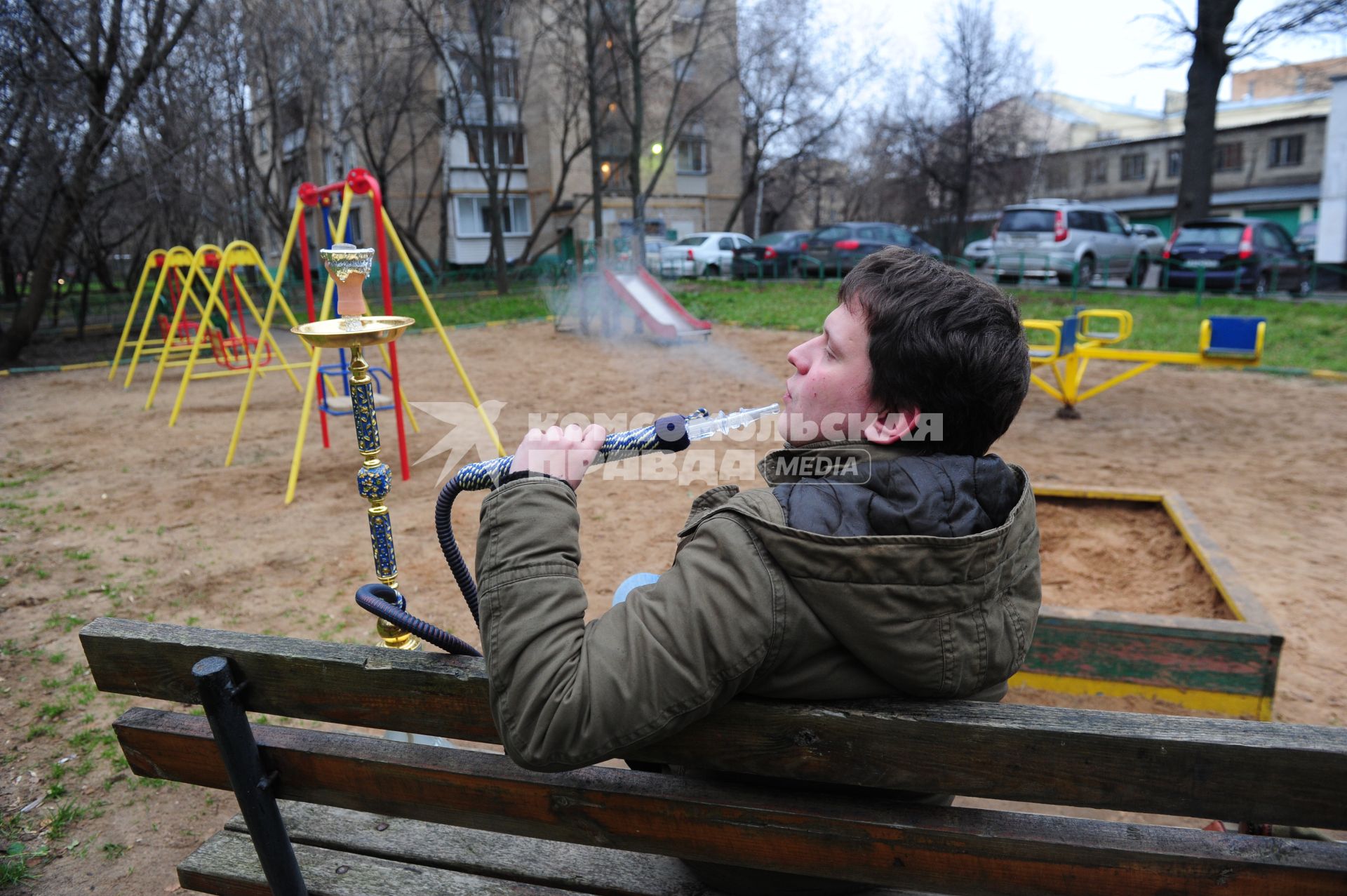 Молодой человек курит кальян на детской полщадке.