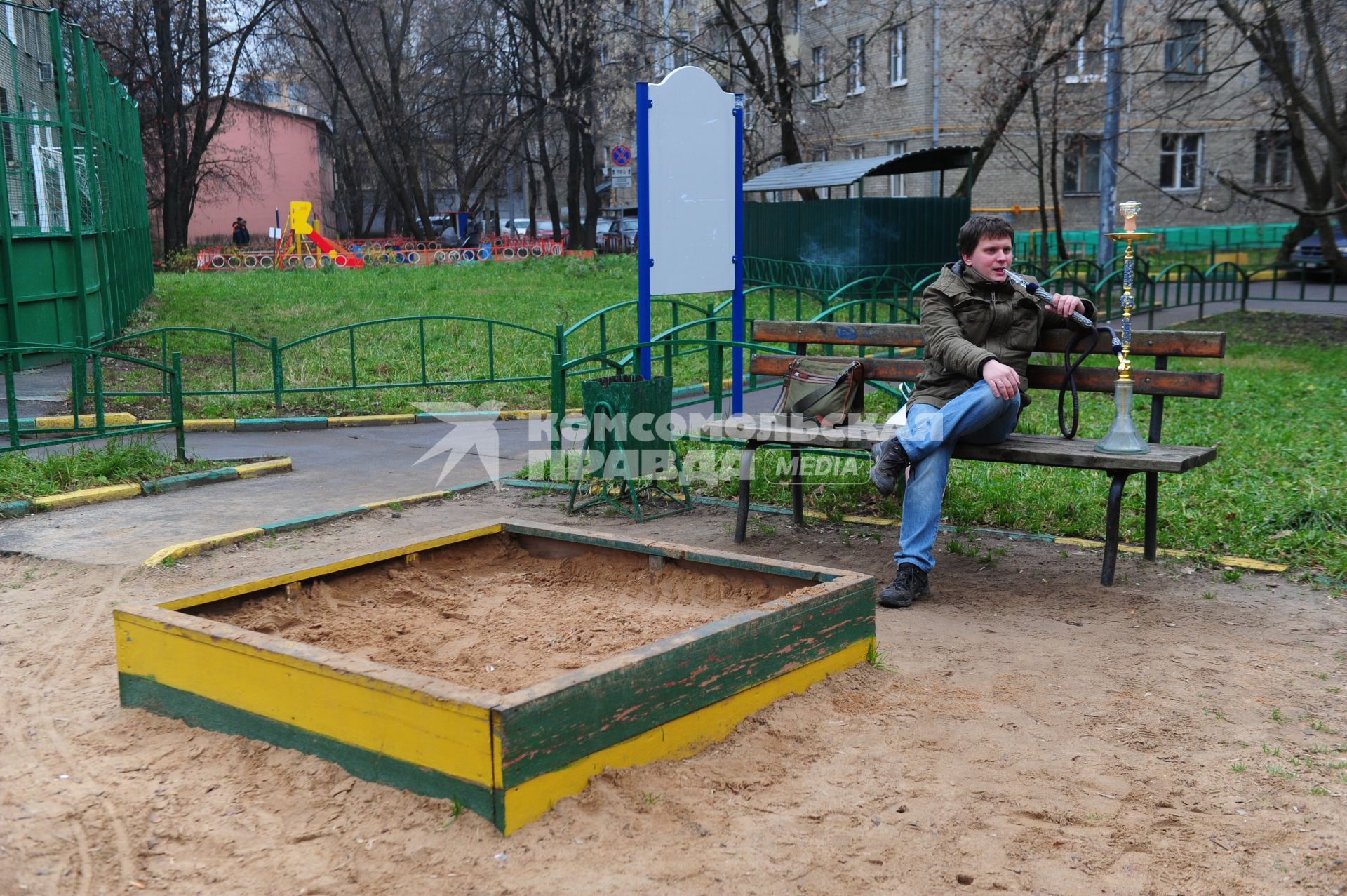 Молодой человек курит кальян на детской полщадке.