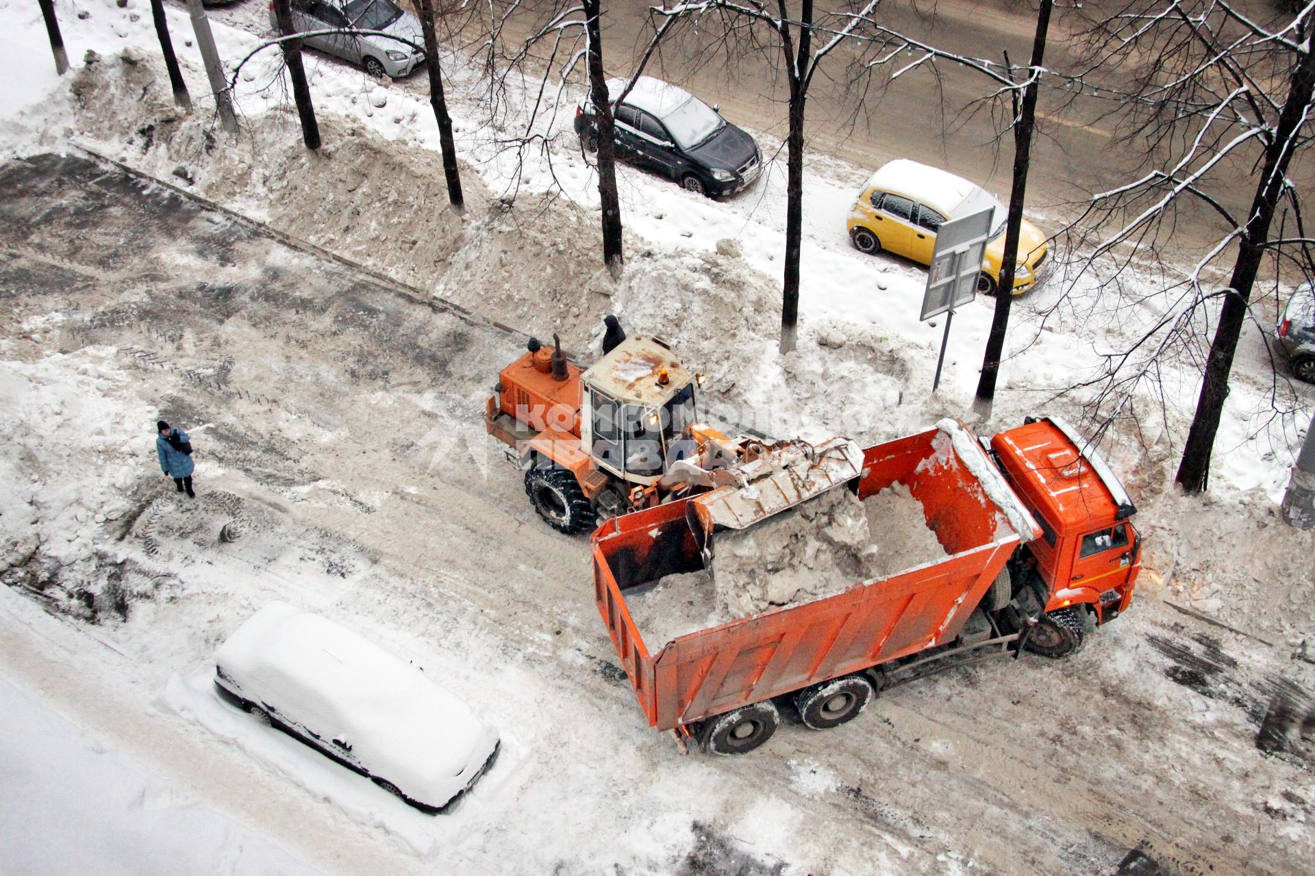 Трактор загружает снег в грузовик `Камаз`.