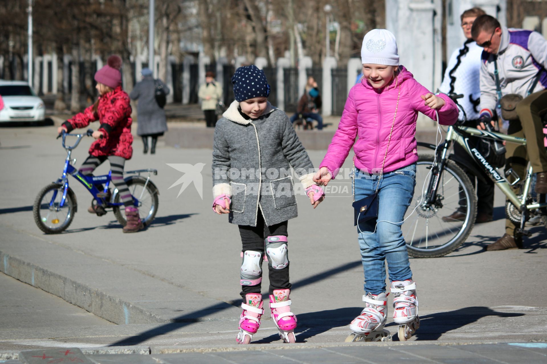 Дети на роликахи велосипедах гуляют на улице.