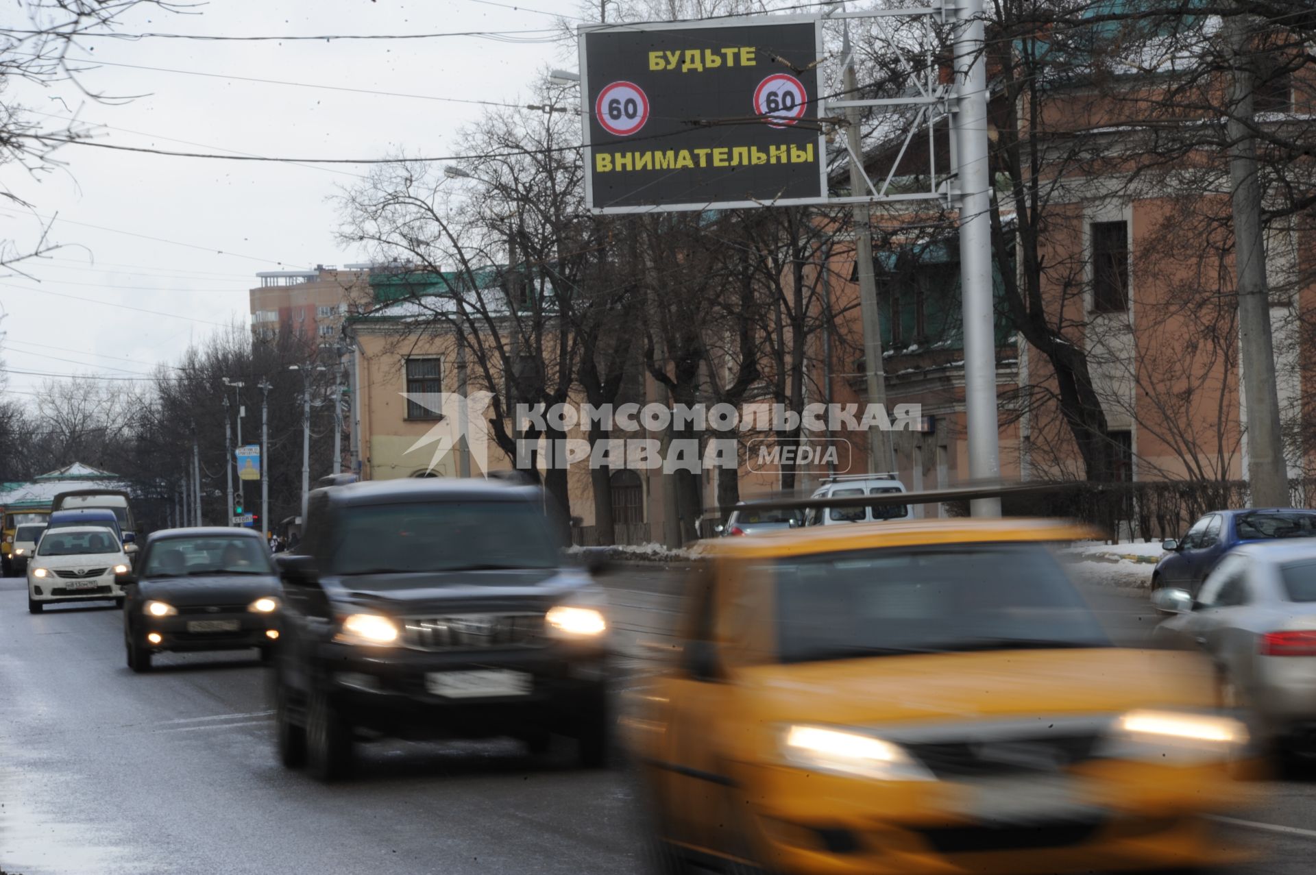 Дорожное табло `Будьте внимательны`. Автомобили с включенными фарами.