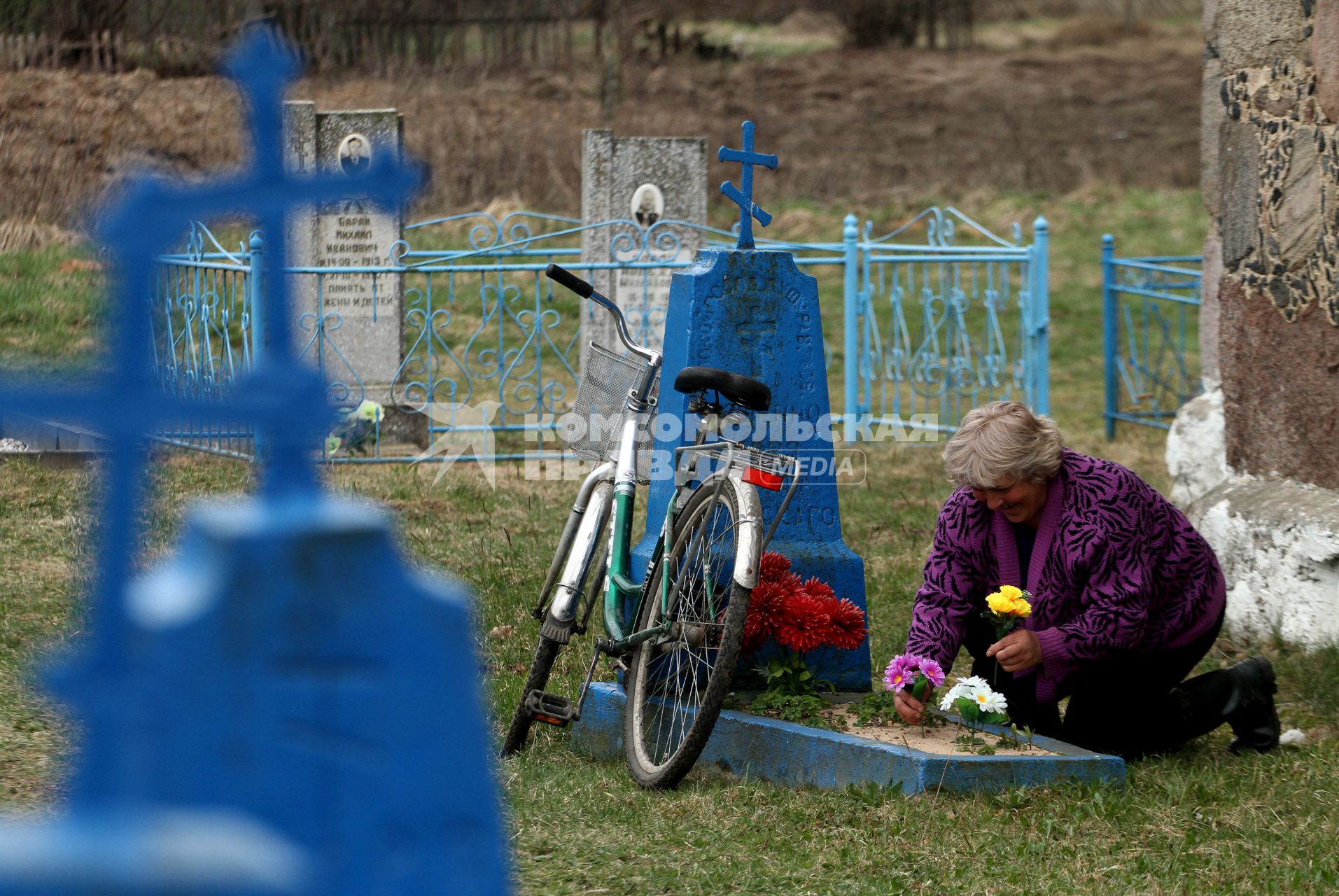 Женщина украшает цветами могилу на кладбище.