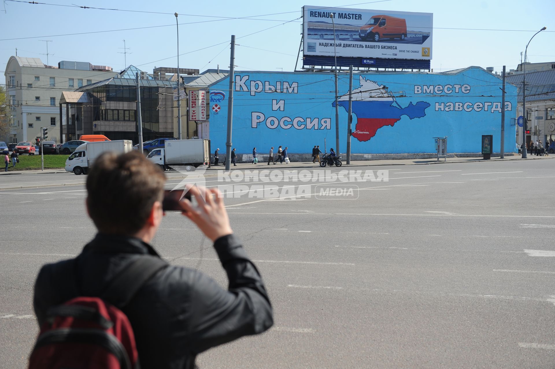 Мужчина фотографирует на мобильный телефон картину на стене здания на Таганской площади, созданную активистами партии `Единая Россия` - `Крым и Россия - вместе навсегда`.