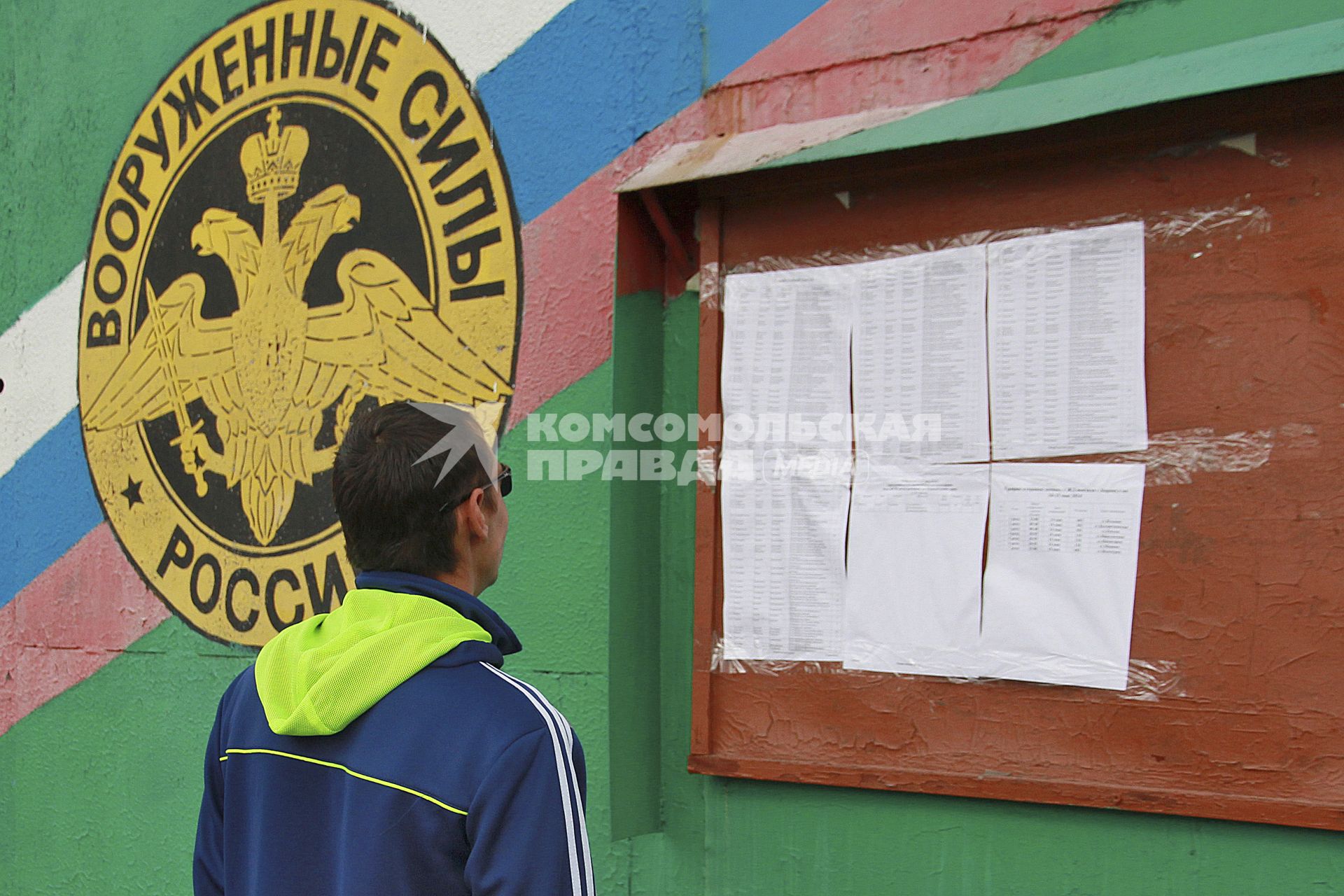 Мужчина у доски объявлений на фоне герба вооруженных сил России.