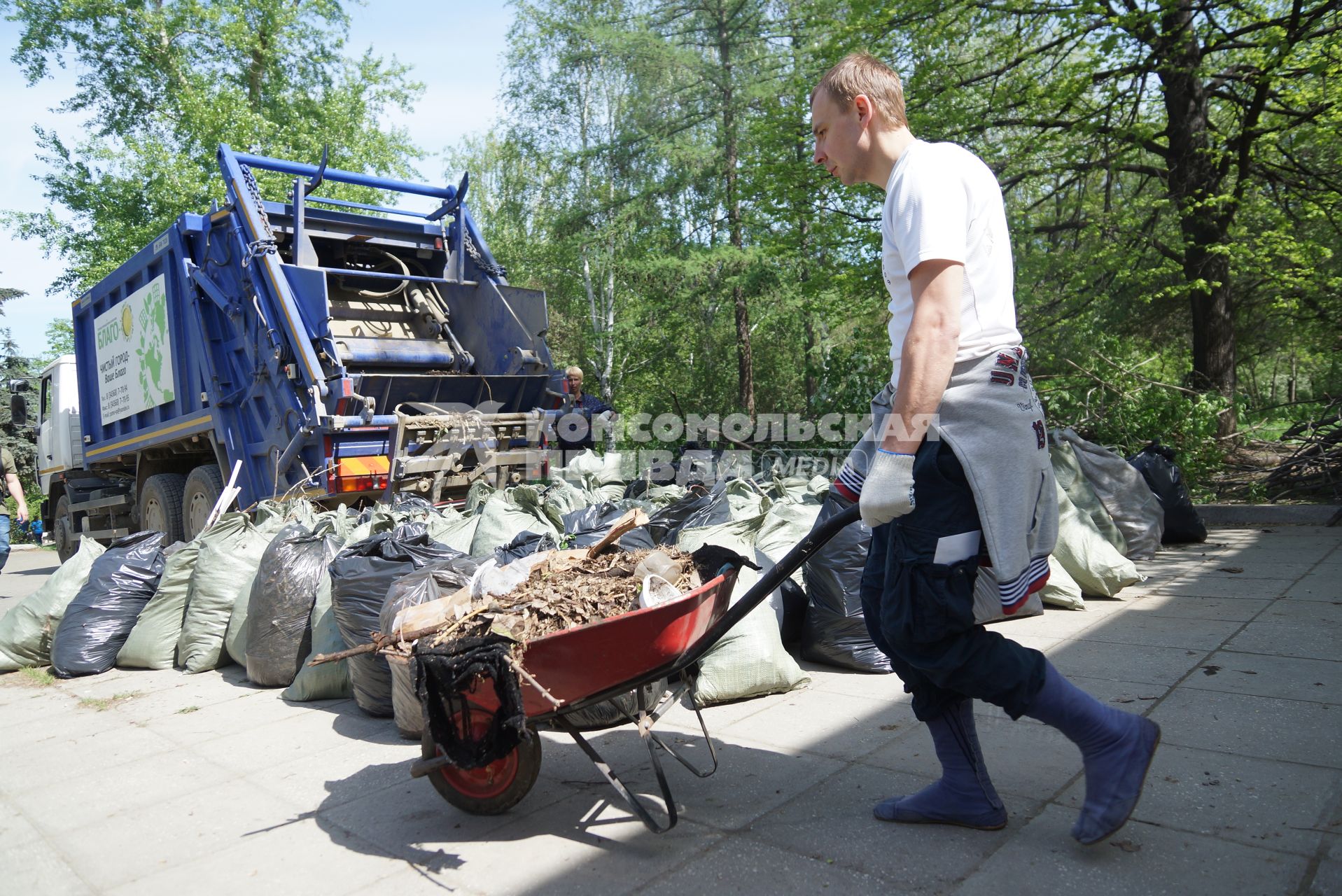 Мужчина катит тележку с мусором мимов мусоровоза и мешков с мусором на субботнике в Харитоновском саду