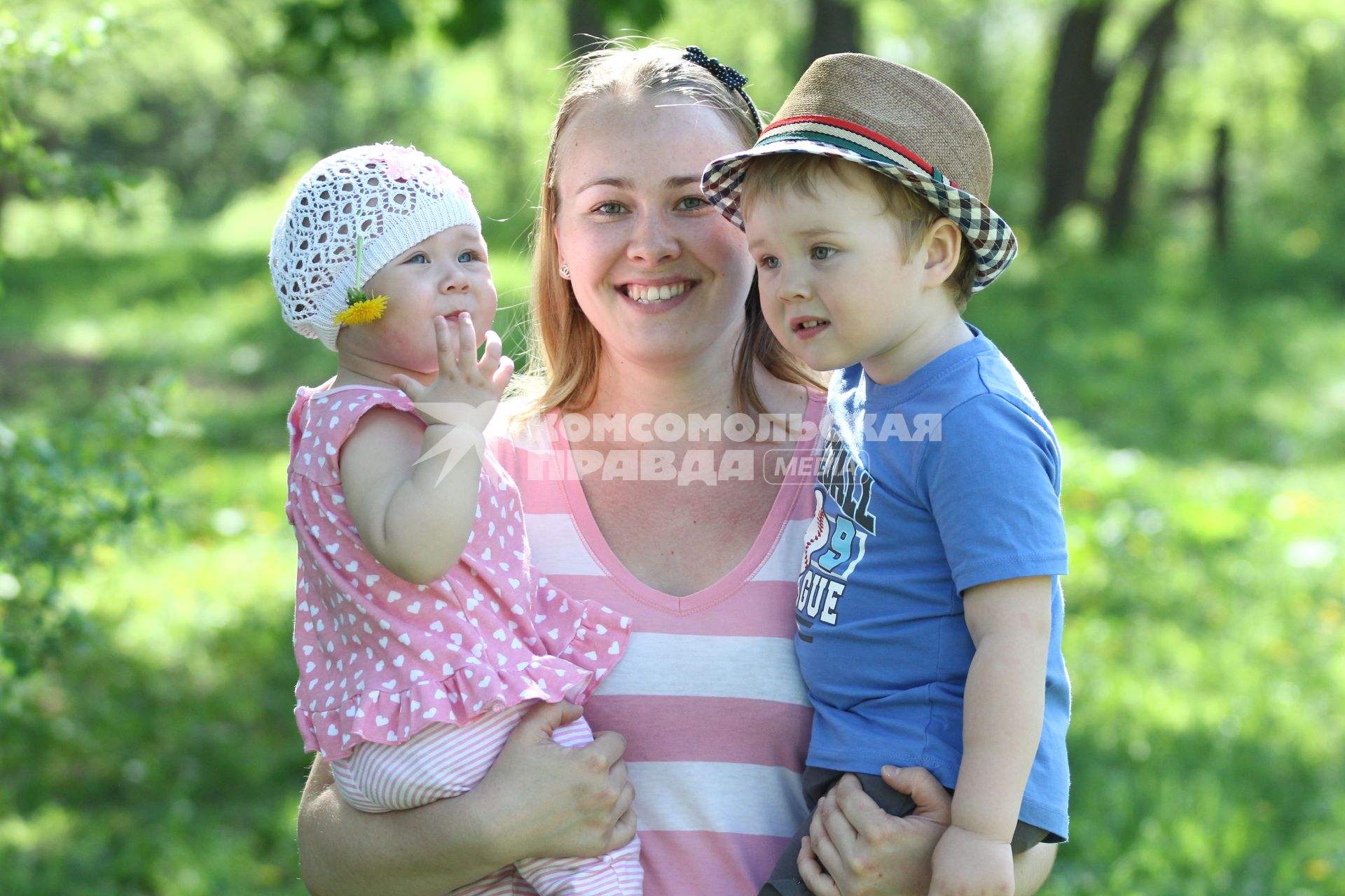 Женщина с двумя детьми на руках летом в парке.