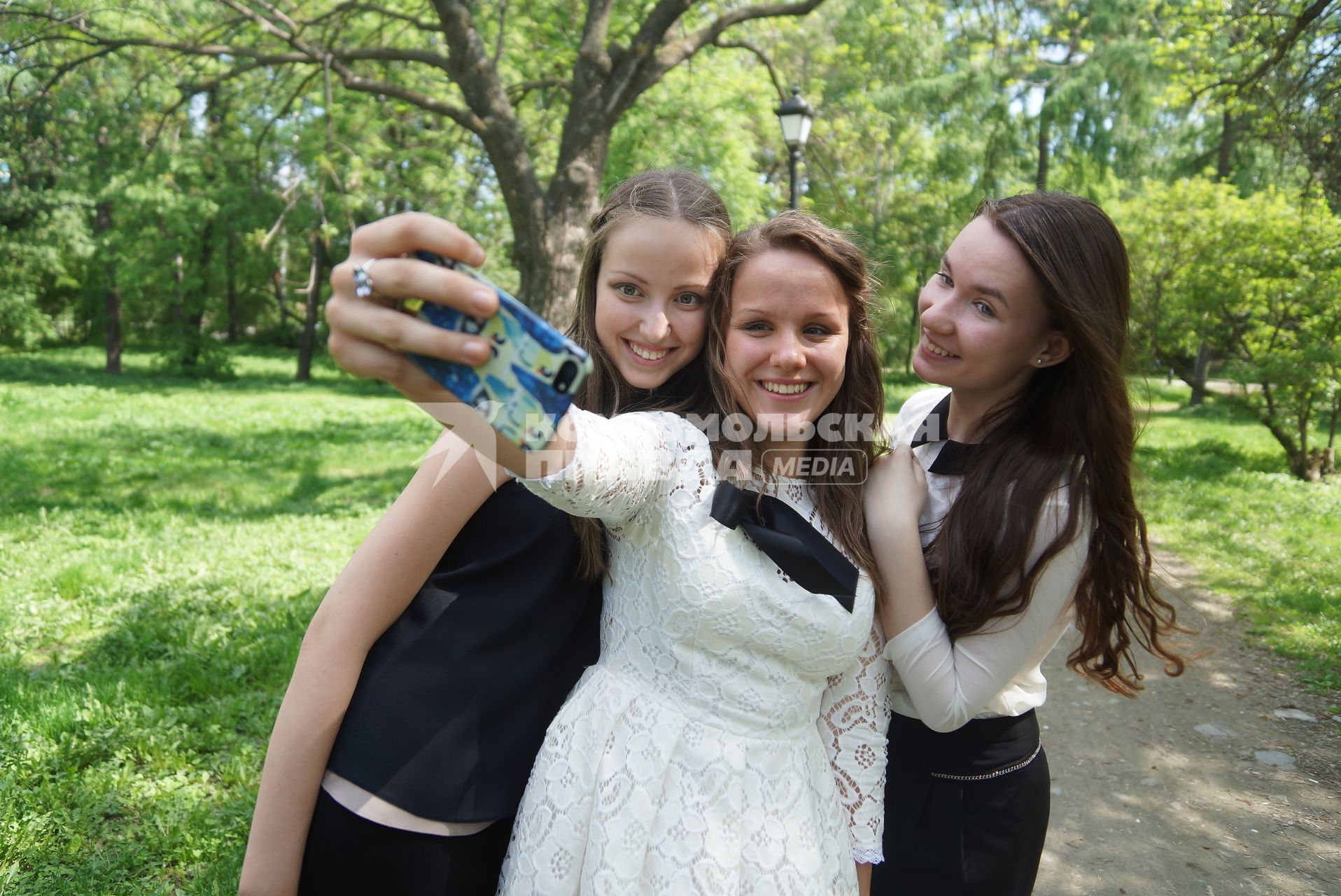 Выпускницы в парке фотографируются на телефон во время празднования последнего звонка в школах