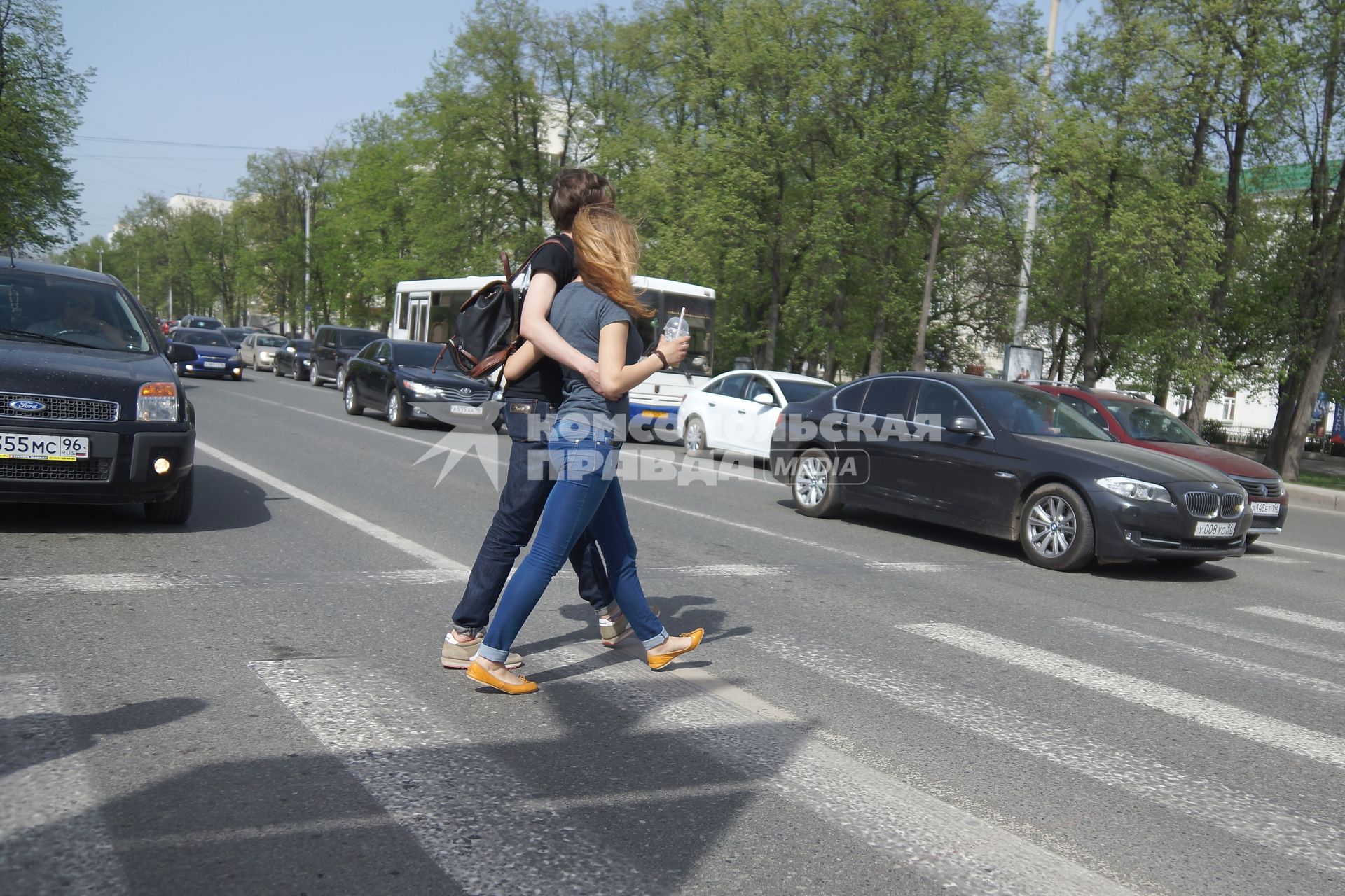 Влюбленная пара обнявшись переходят дорогу по пешеходному переходу