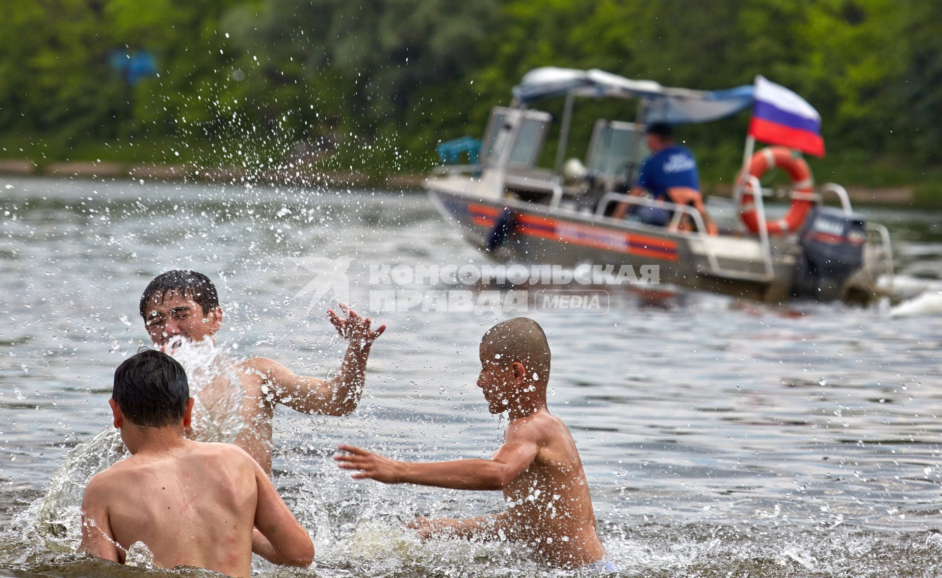 Дети играют в воде на фоне проходящего спасательного катера.