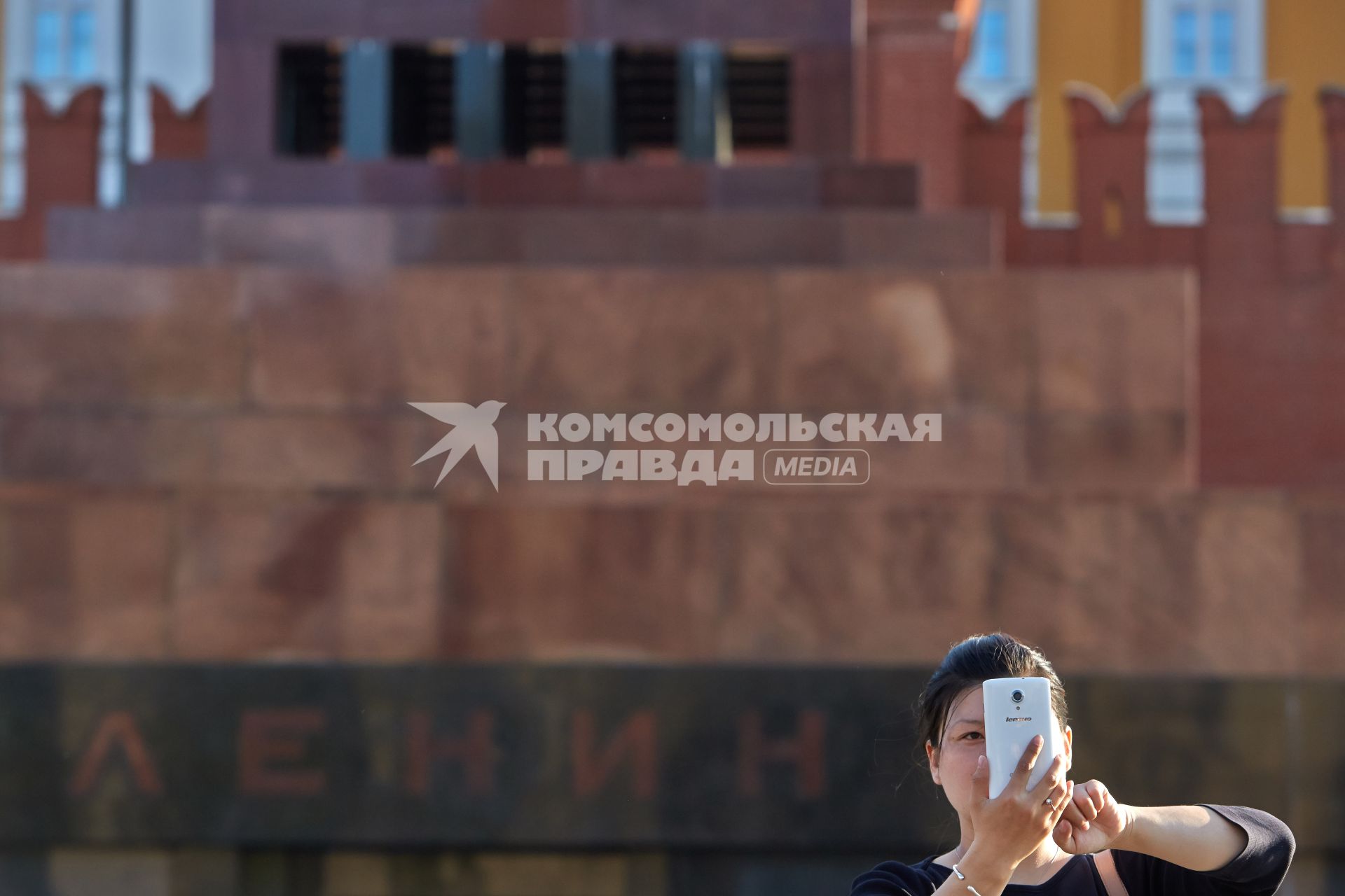 Женщина с азиатской внешностью фотографирует на телефон на против мавзолея.