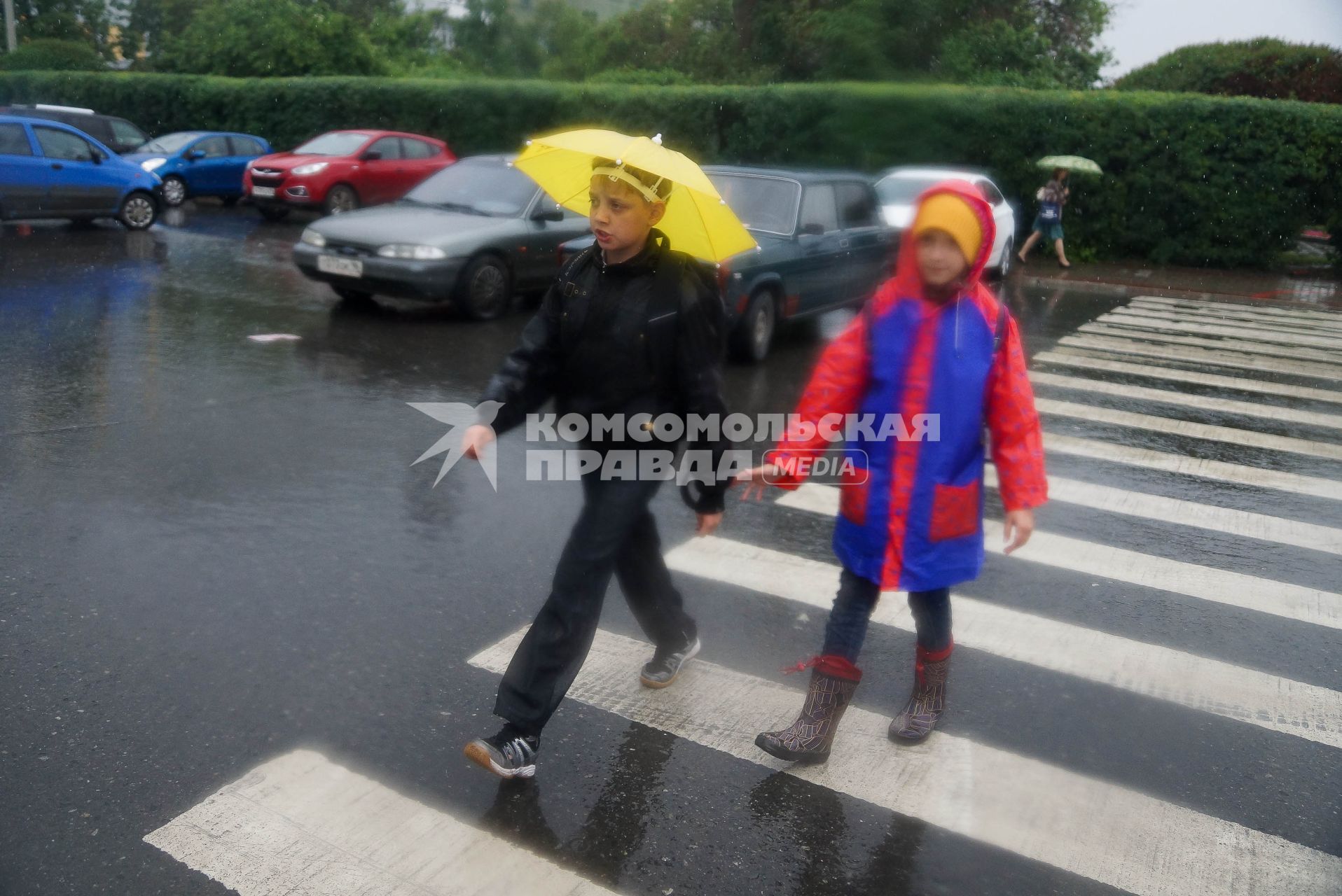 Мальчик с зонтиком на голове идет через  дорогу идет под дождем