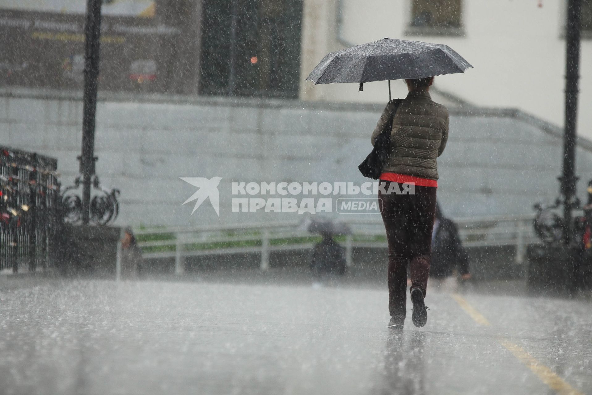 Девушка под зонтом идет по мосту во время дождя