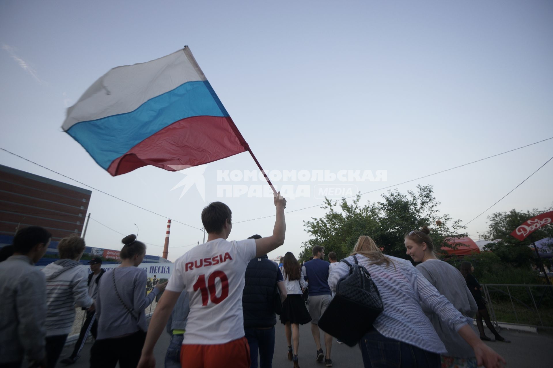 Мужчина в белой фетболке с надписью Россия Russia размахивает флагом России по пути в фан-зону перед матчем Россия - бельгия