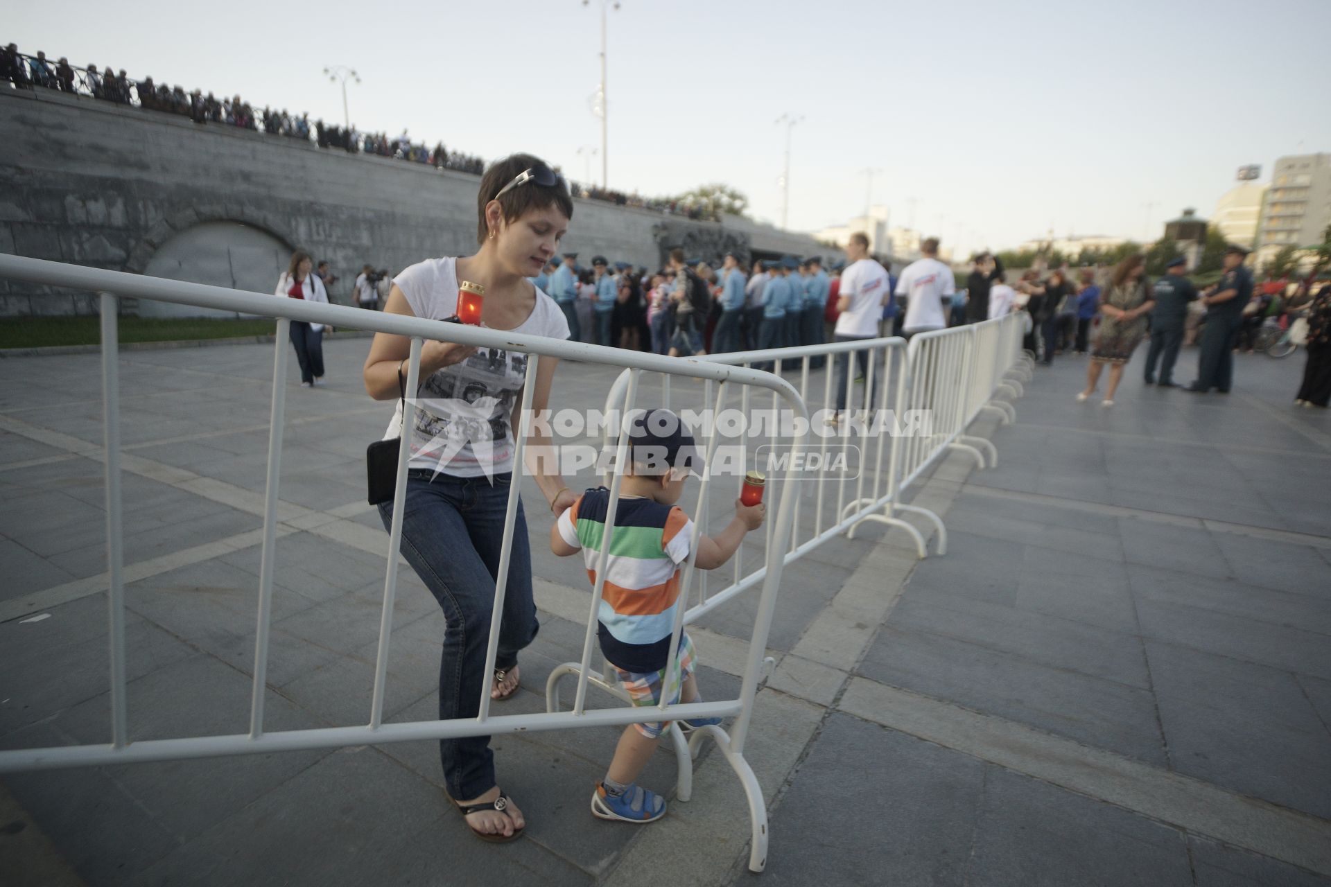 женщина с зажженой лампадой останавливает маленького сына выходащего за ограждение во время провения акции \"Свеча памяти\" в Екатеринбурге