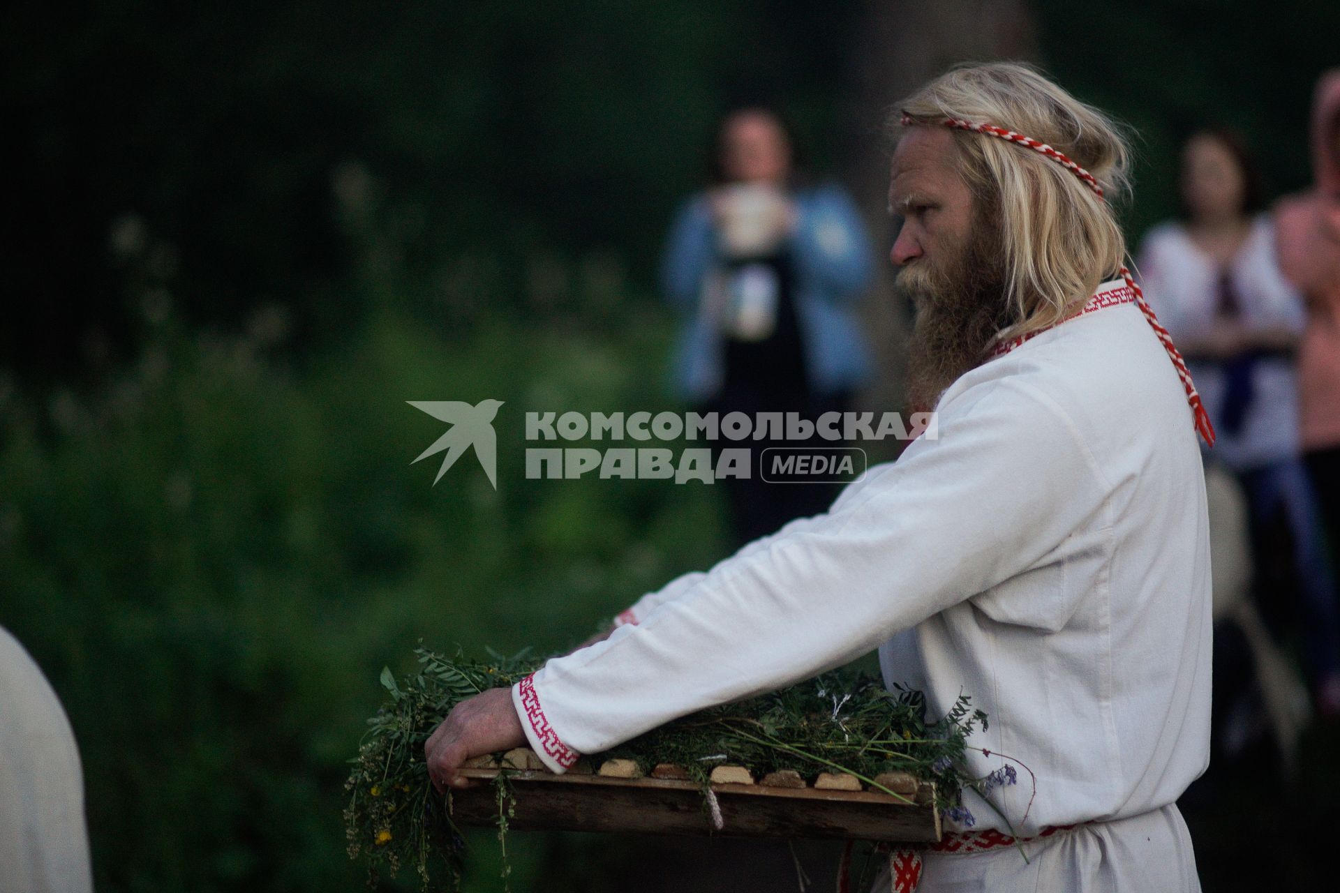 Участник празднования дня Ивана Купала стоит с венком в руках, перед его спуском на воду